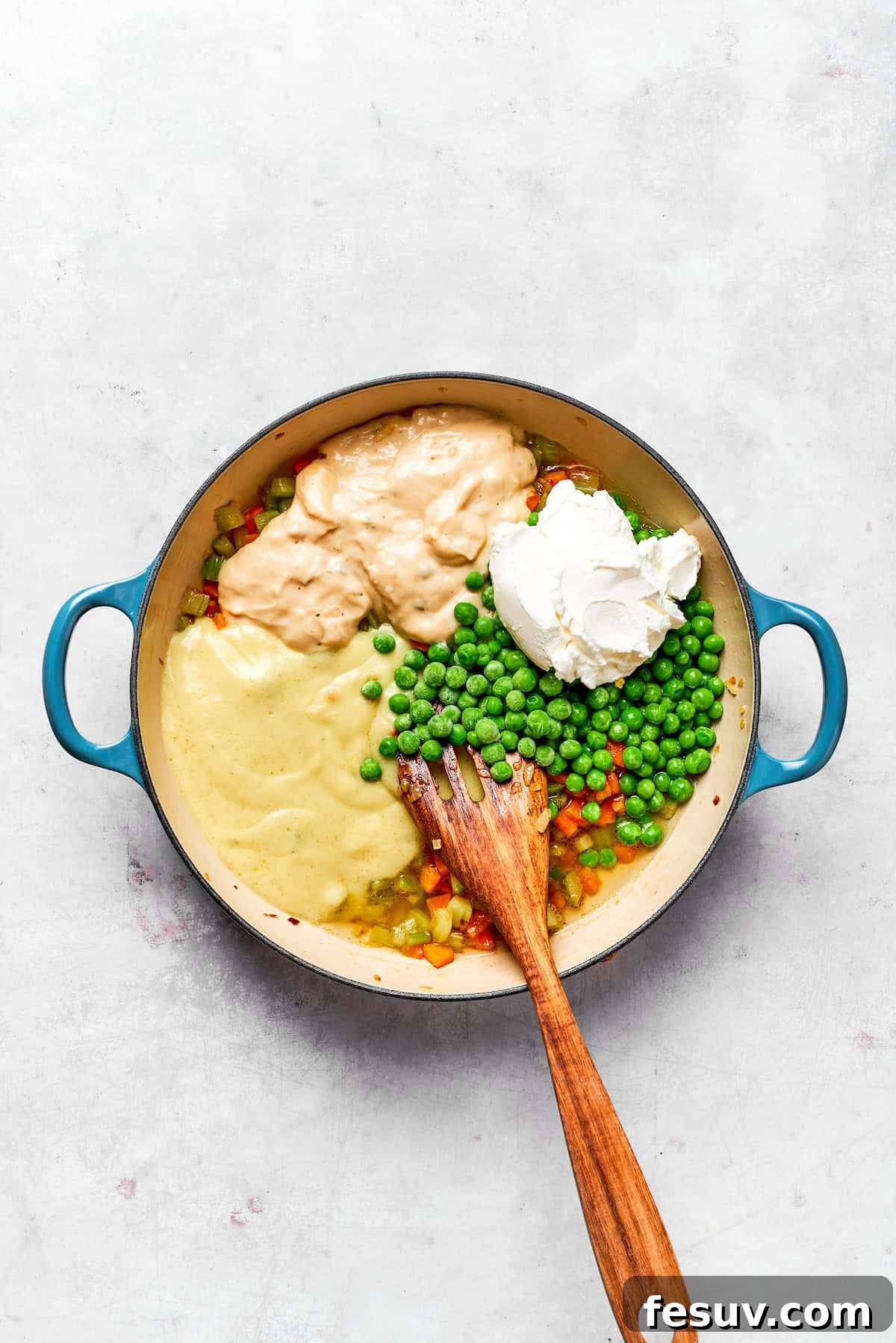 Sour cream, condensed soups, and frozen peas being added to the cooked vegetables in a pot.