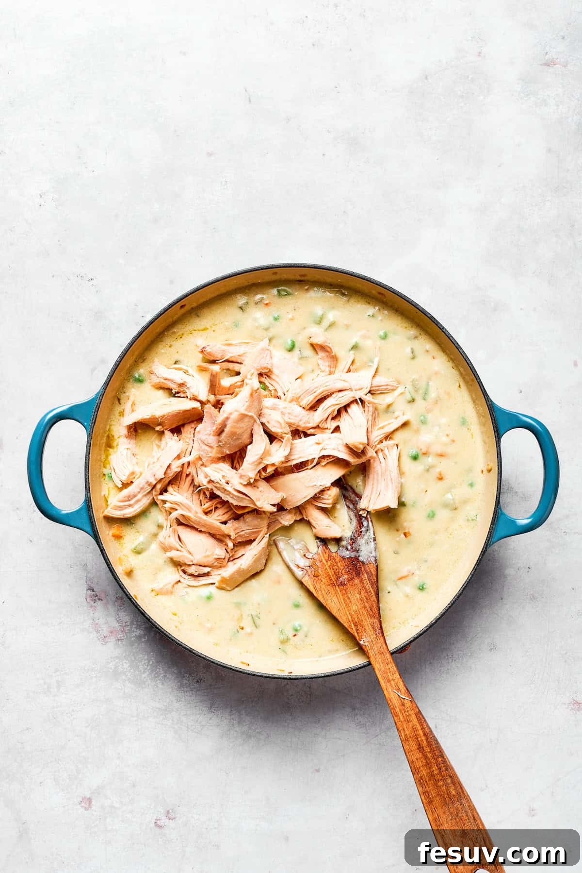 Shredded chicken being mixed into the creamy vegetable filling.