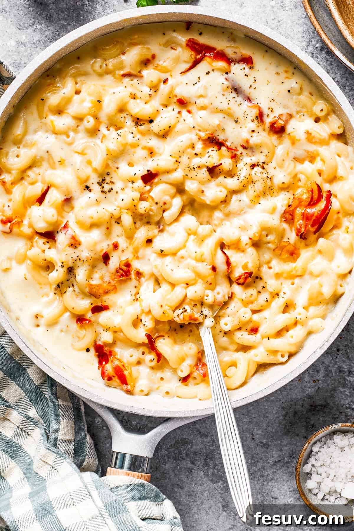 A skillet filled with creamy, cheesy bacon mac and cheese, stirred and ready to serve, with visible crispy bacon pieces.