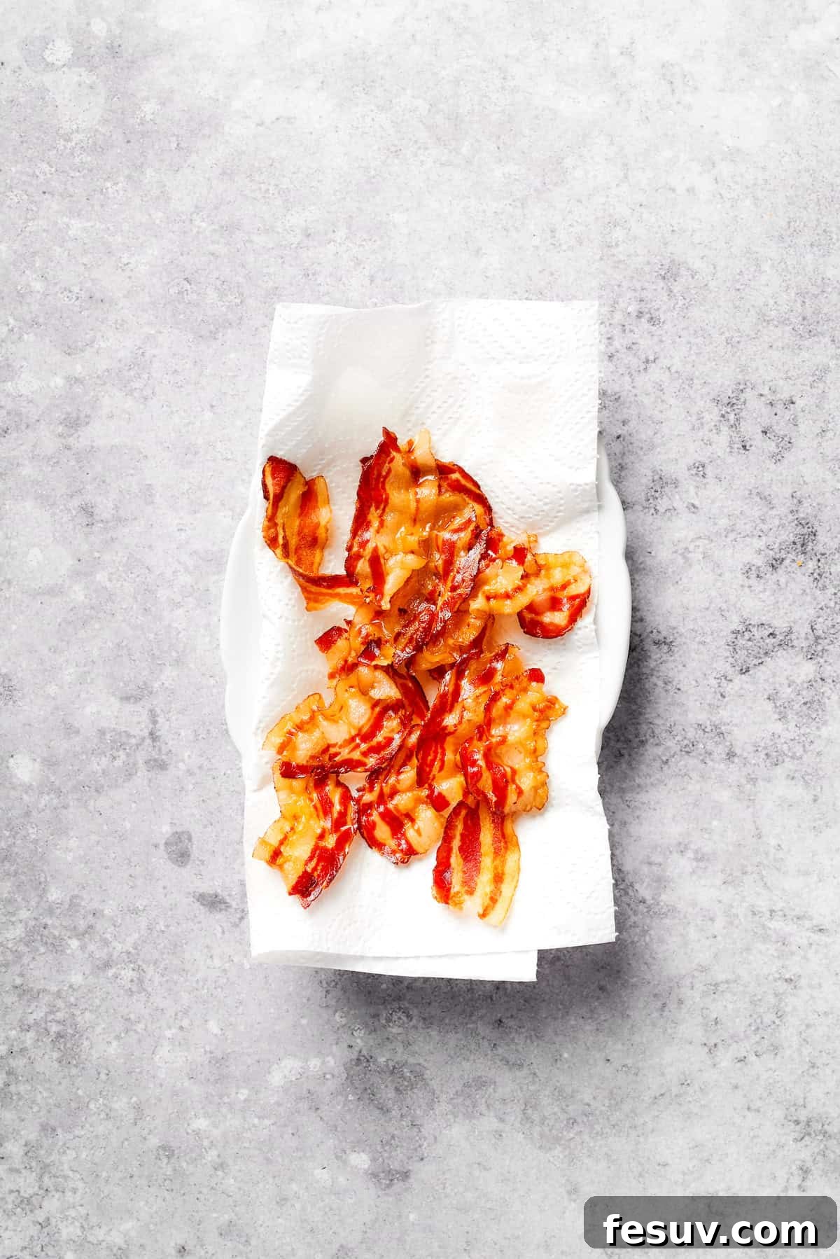 Crispy cooked bacon pieces draining on a paper towel-lined plate, ready for adding to mac and cheese.
