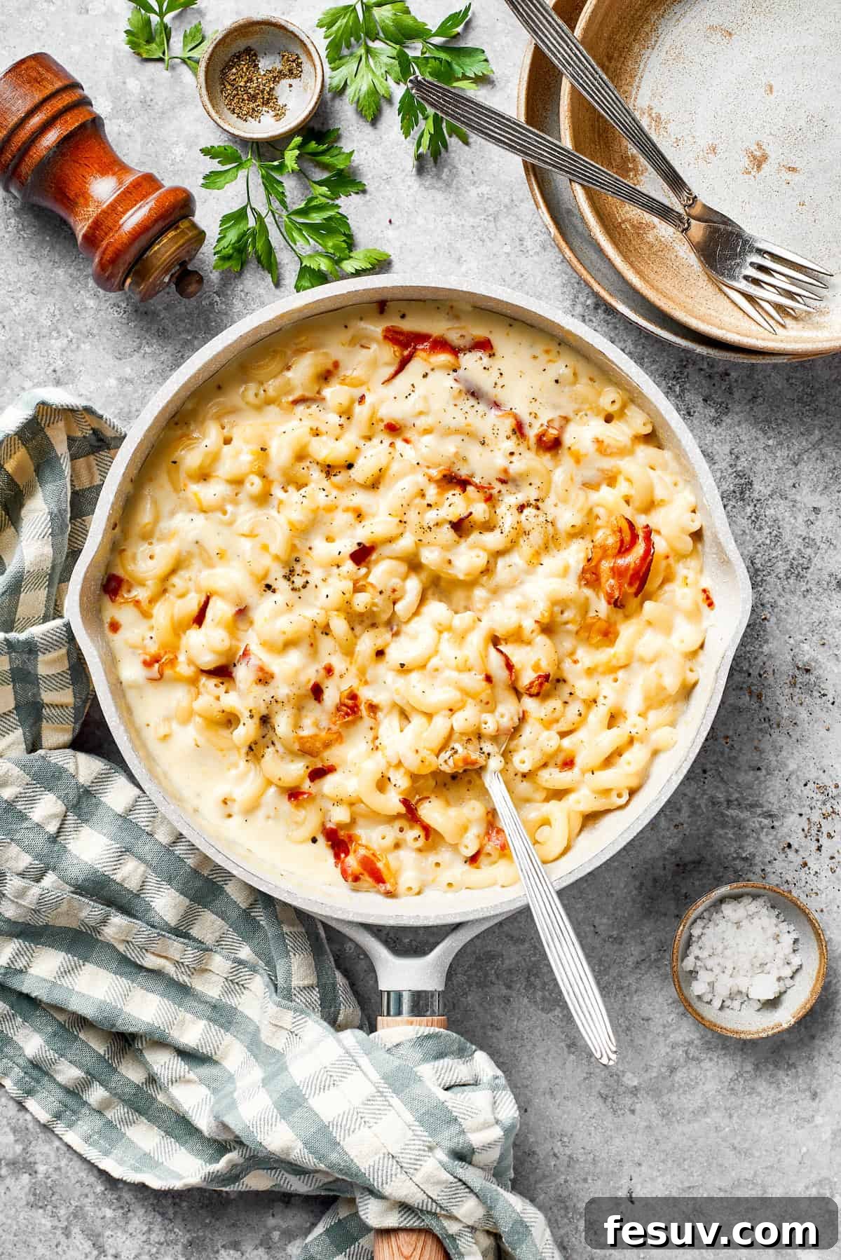 A large pan of freshly made bacon mac and cheese, perfectly mixed and ready to be served with a spoon resting in the dish.