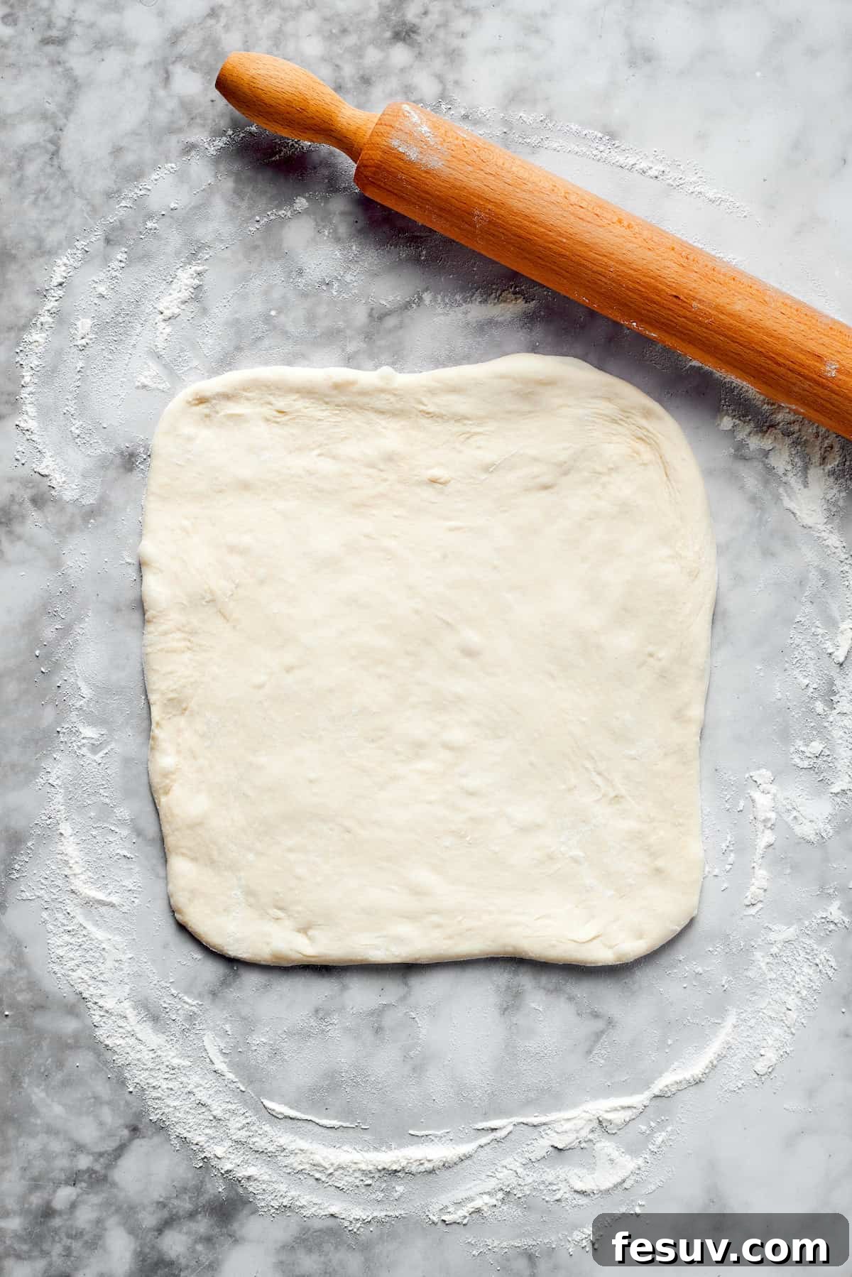 Pizza dough rolled out into a neat rectangular shape on a floured surface.