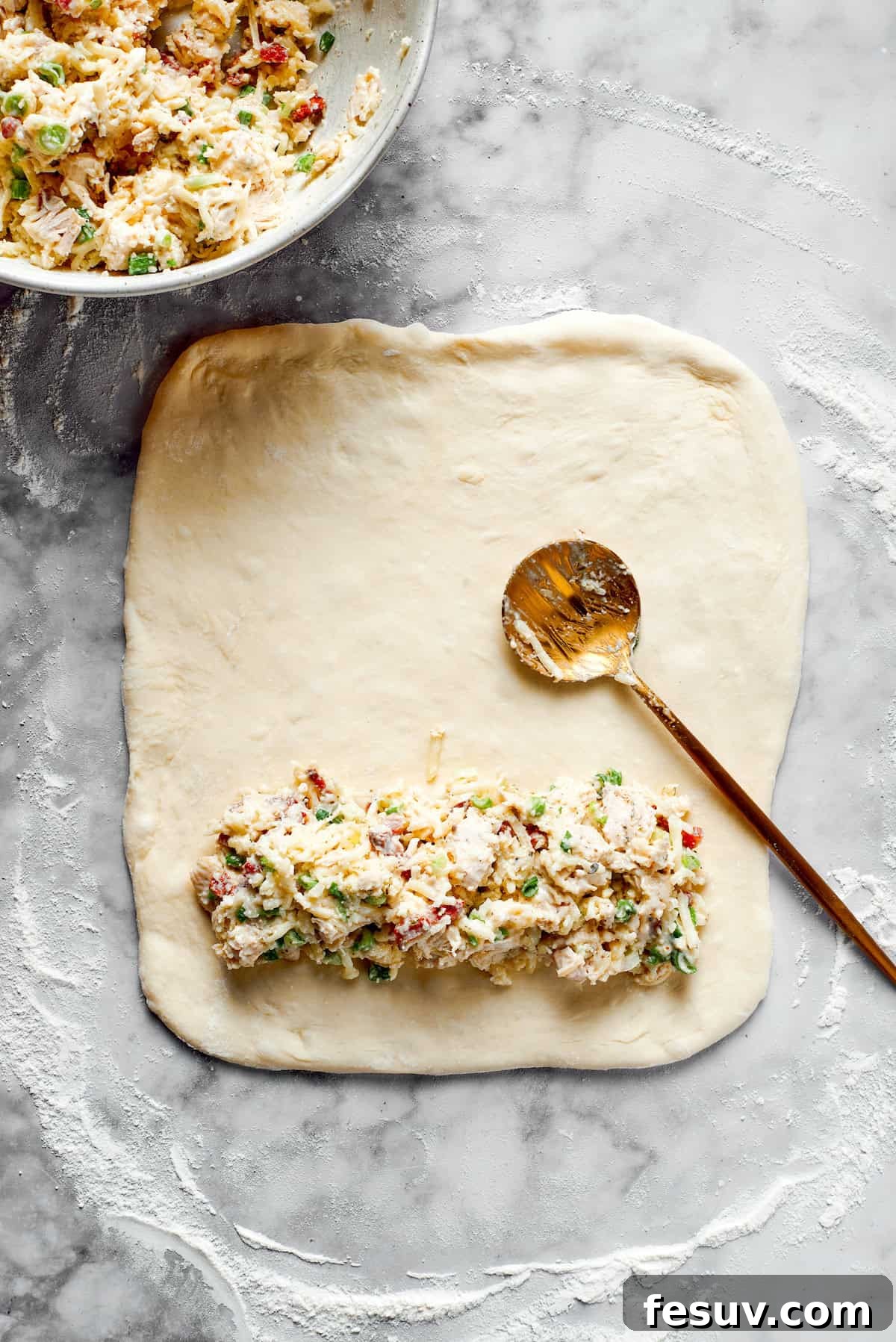 A small portion of chicken bake filling spread along one edge of the rolled-out pizza dough.