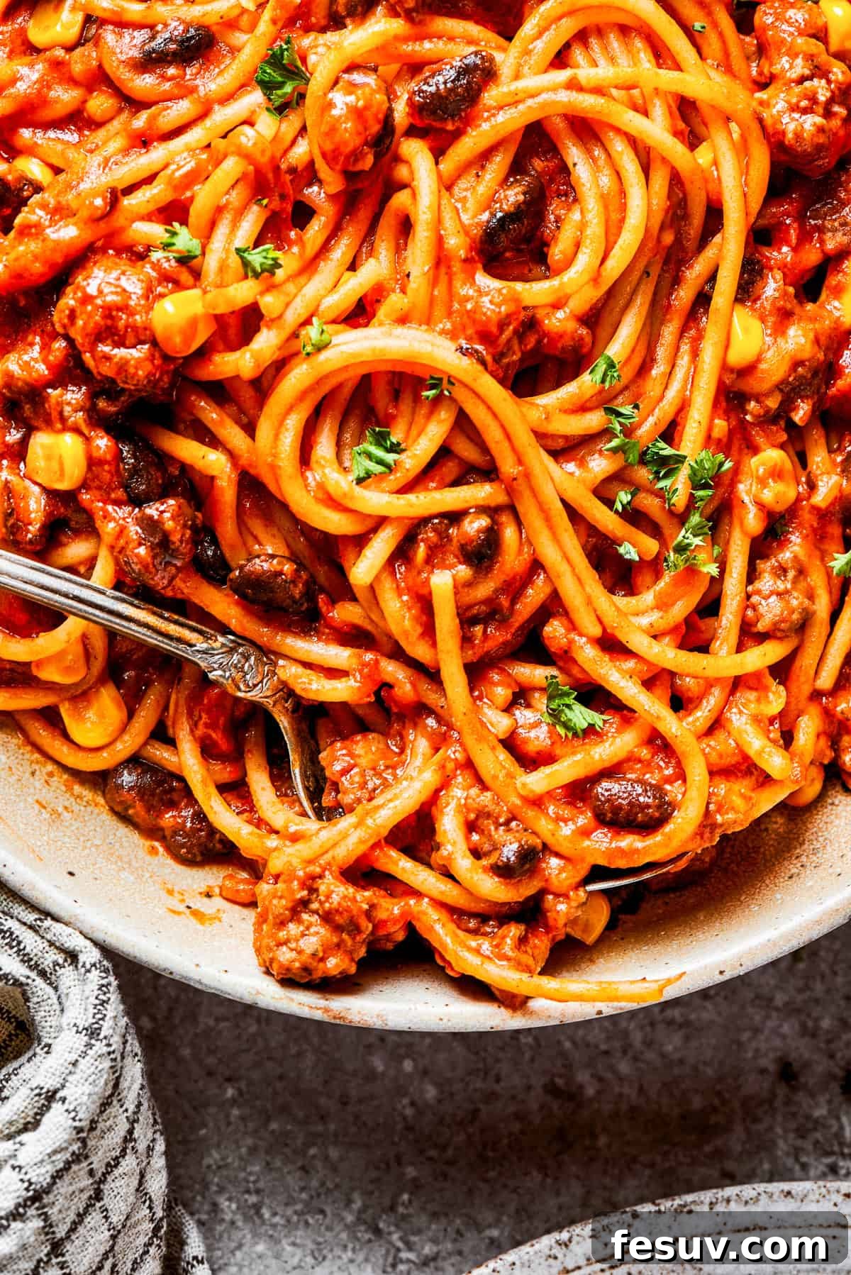 Hearty Mexican spaghetti loaded with ground beef, sweet corn, black beans, and cheese. A perfect taco-flavored pasta dinner! Close-up image of cooked spaghetti in a rich, cheesy sauce with corn and beans.