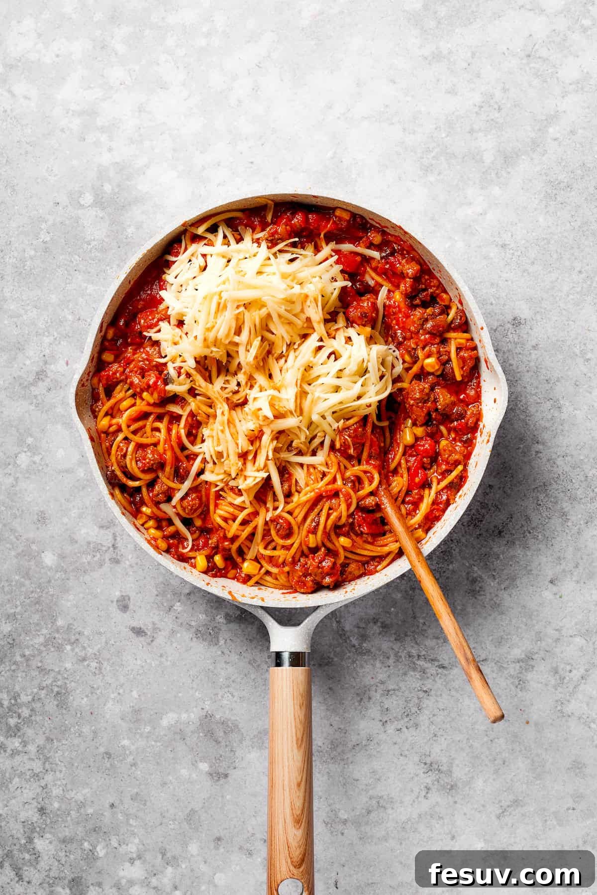 Adding and melting a blend of cheeses into the Mexican spaghetti for a creamy, indulgent finish. Shredded Pepper Jack and Monterey Jack cheeses being stirred into the hot Mexican spaghetti.