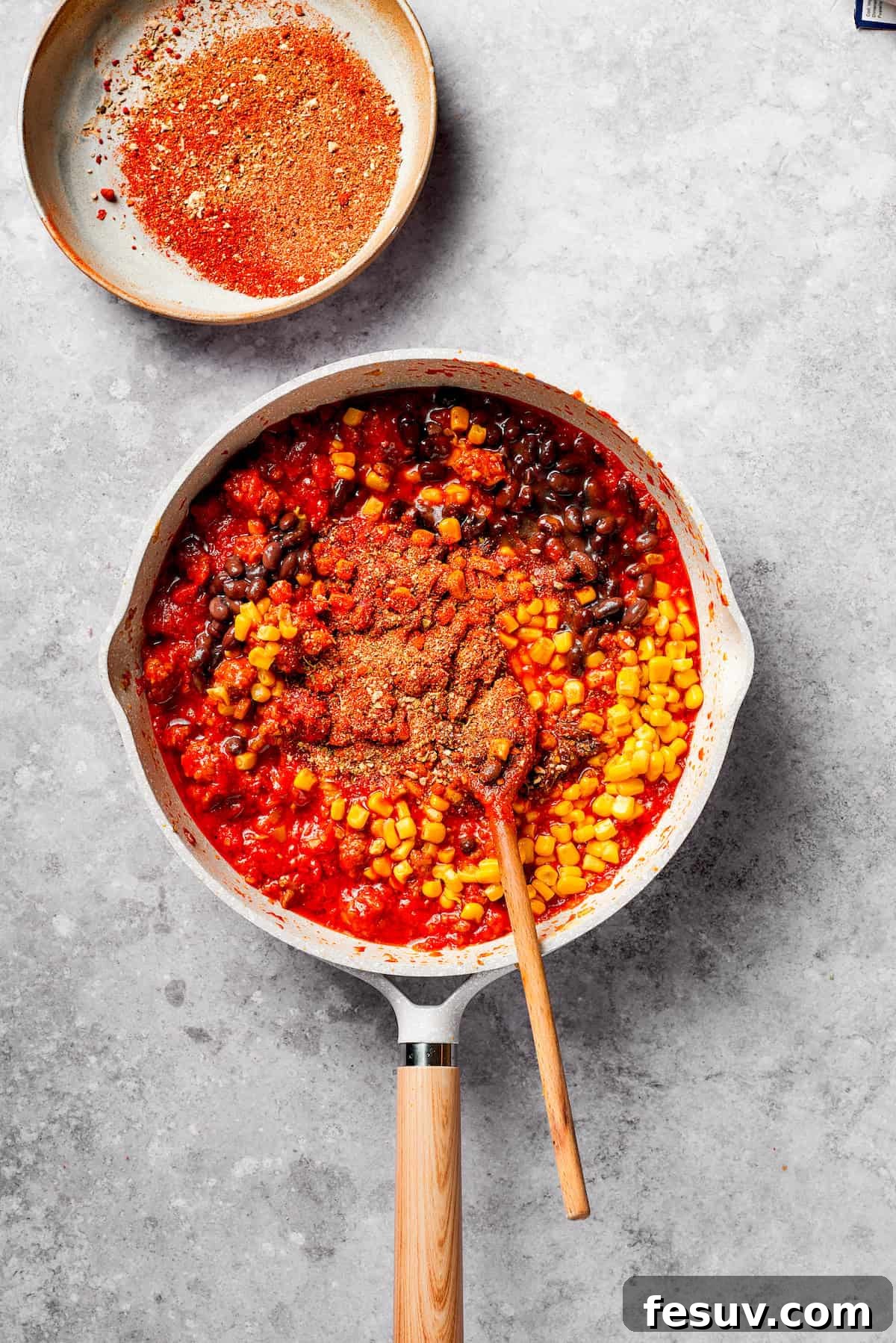 Stirring in black beans and corn to the robust Mexican spaghetti sauce. The ground beef mixture in a pan, now incorporating black beans and corn, being stirred.