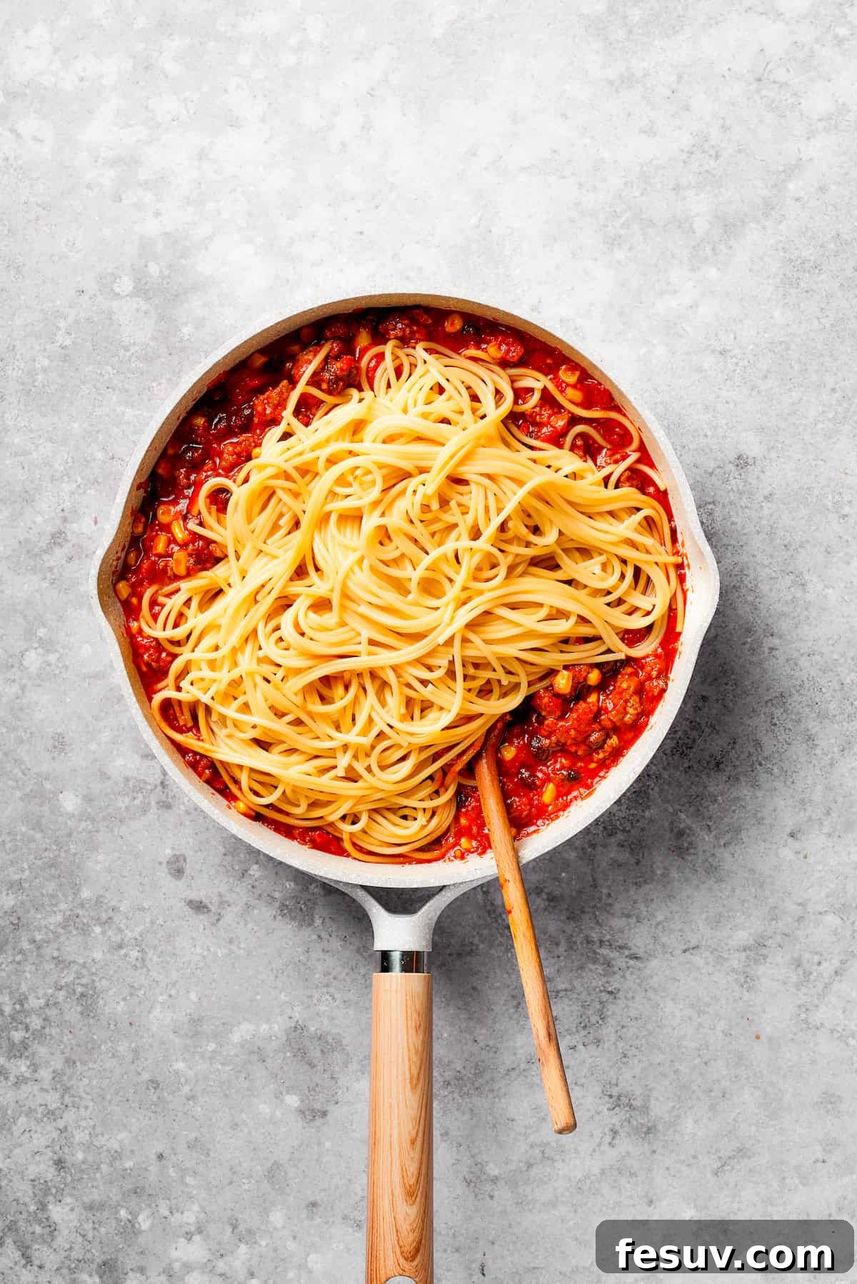 Mixing freshly cooked spaghetti into the savory Mexican meat sauce for a delightful fusion. Cooked spaghetti being gently mixed into the vibrant Mexican-style meat sauce.