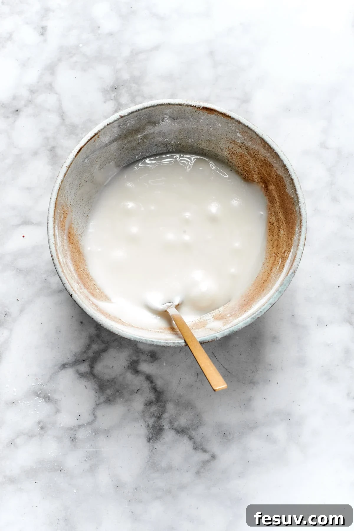 The cutest Melted Snowman Cookies top buttery homemade sugar cookies with a thick vanilla frosting and a fluffy marshmallow! Smooth white vanilla icing being mixed in a bowl, reaching the perfect consistency for spreading.