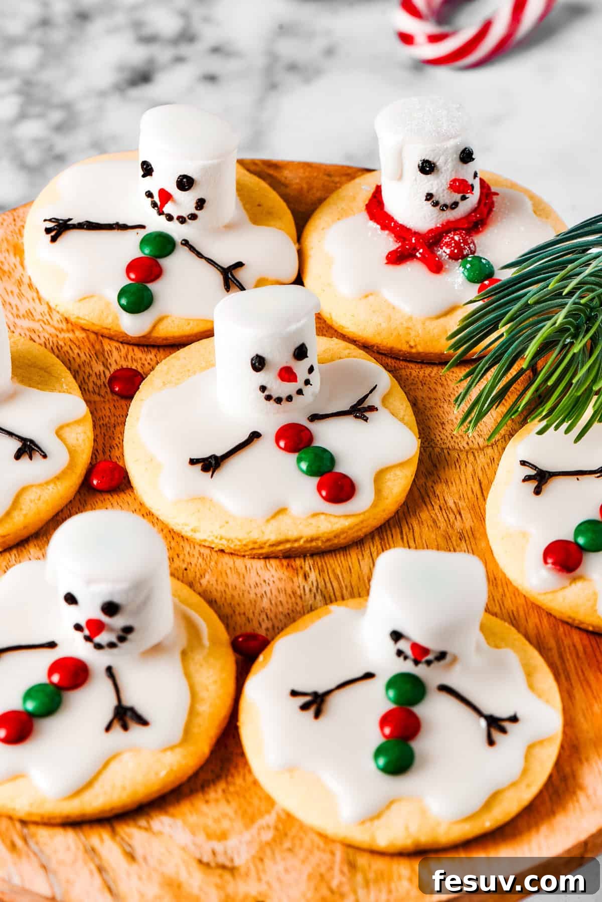 The cutest Melted Snowman Cookies top buttery homemade sugar cookies with a thick vanilla frosting and a fluffy marshmallow! A delightful array of melted snowman cookies carefully arranged on a rustic wooden tray.