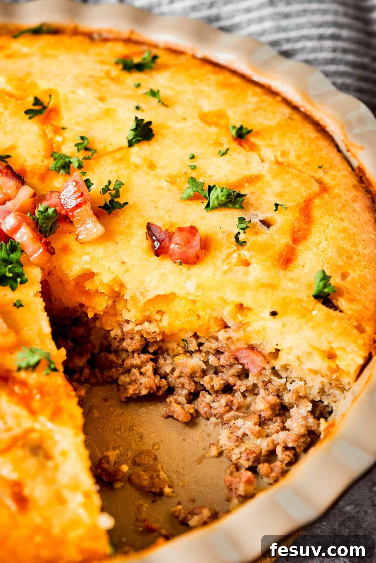 Close-up photo of a cheeseburger pie with a piece of pie cut out to expose the ground meat and melted cheese, showcasing its hearty layers.