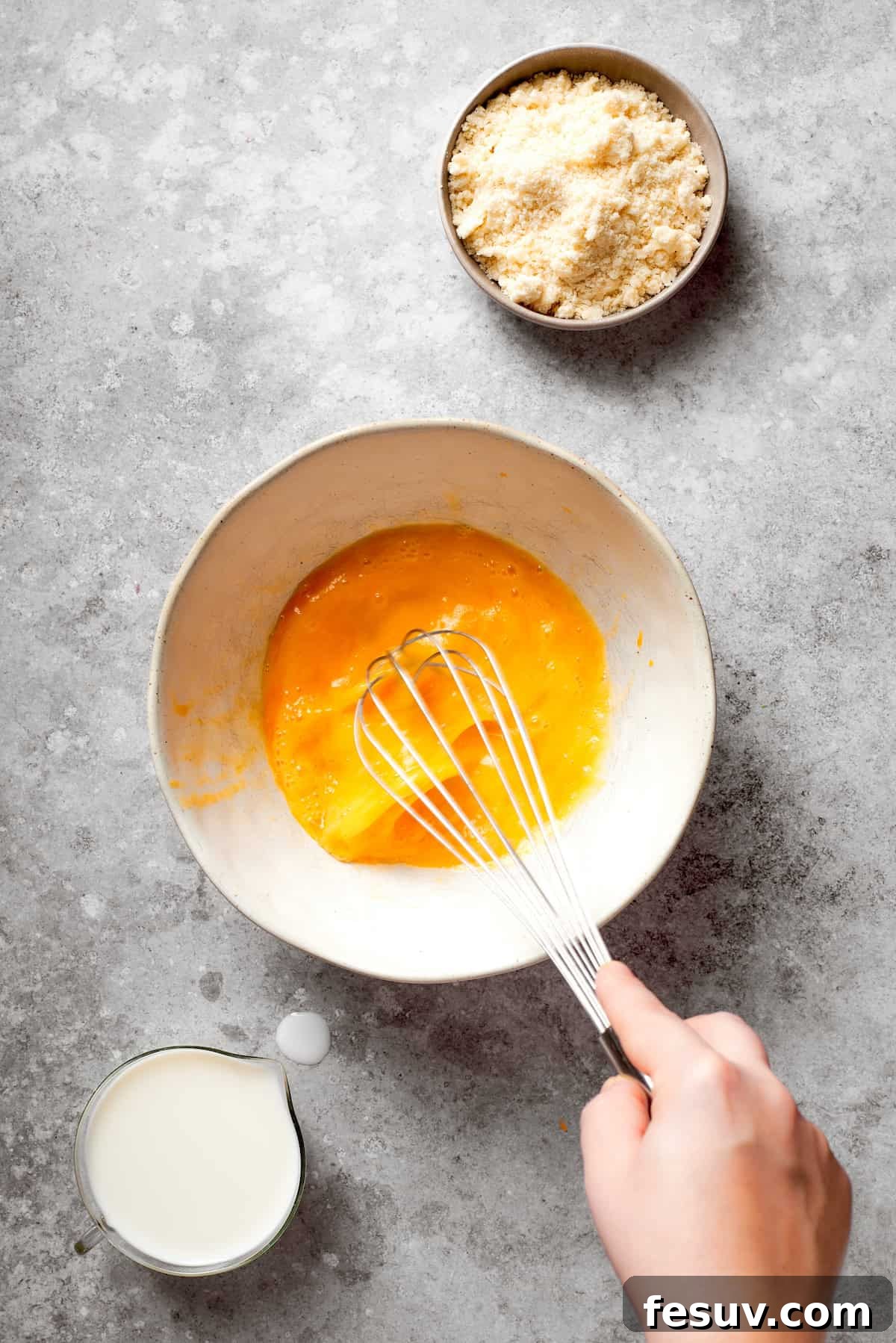 A hand vigorously whisking eggs in a bowl until they are smooth and well combined.