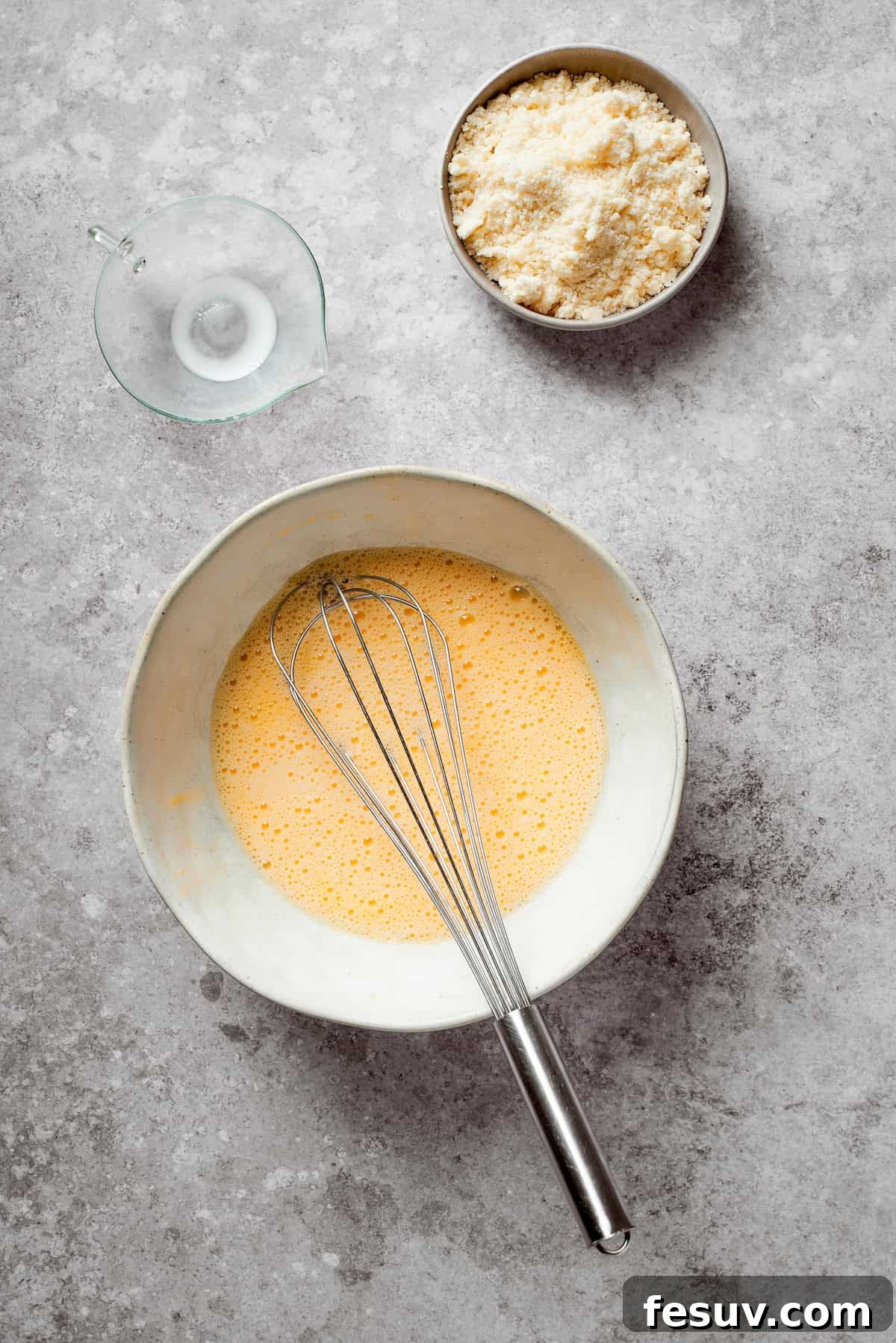 Milk being poured into a bowl with whisked eggs, ready to be combined for the pie's biscuit crust.