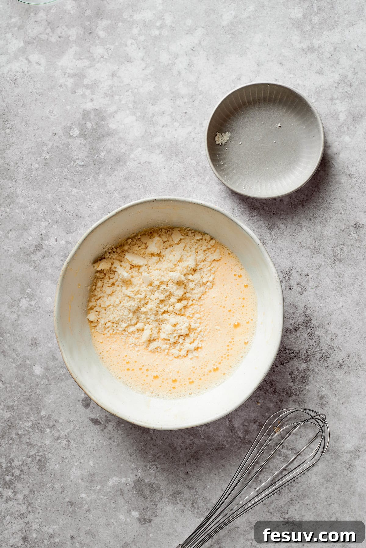 Baking mix (like Bisquick) being mixed into the wet ingredients in a bowl to form the biscuit batter.