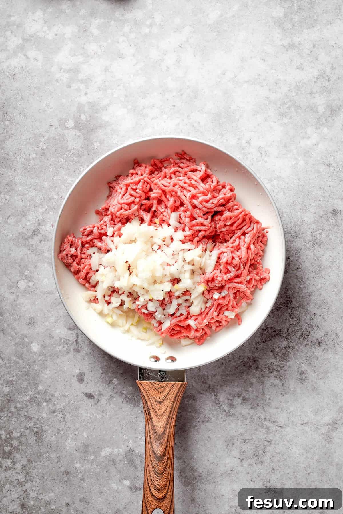 Ground beef and finely diced onion added to the same skillet after bacon has been cooked, ready to be browned.