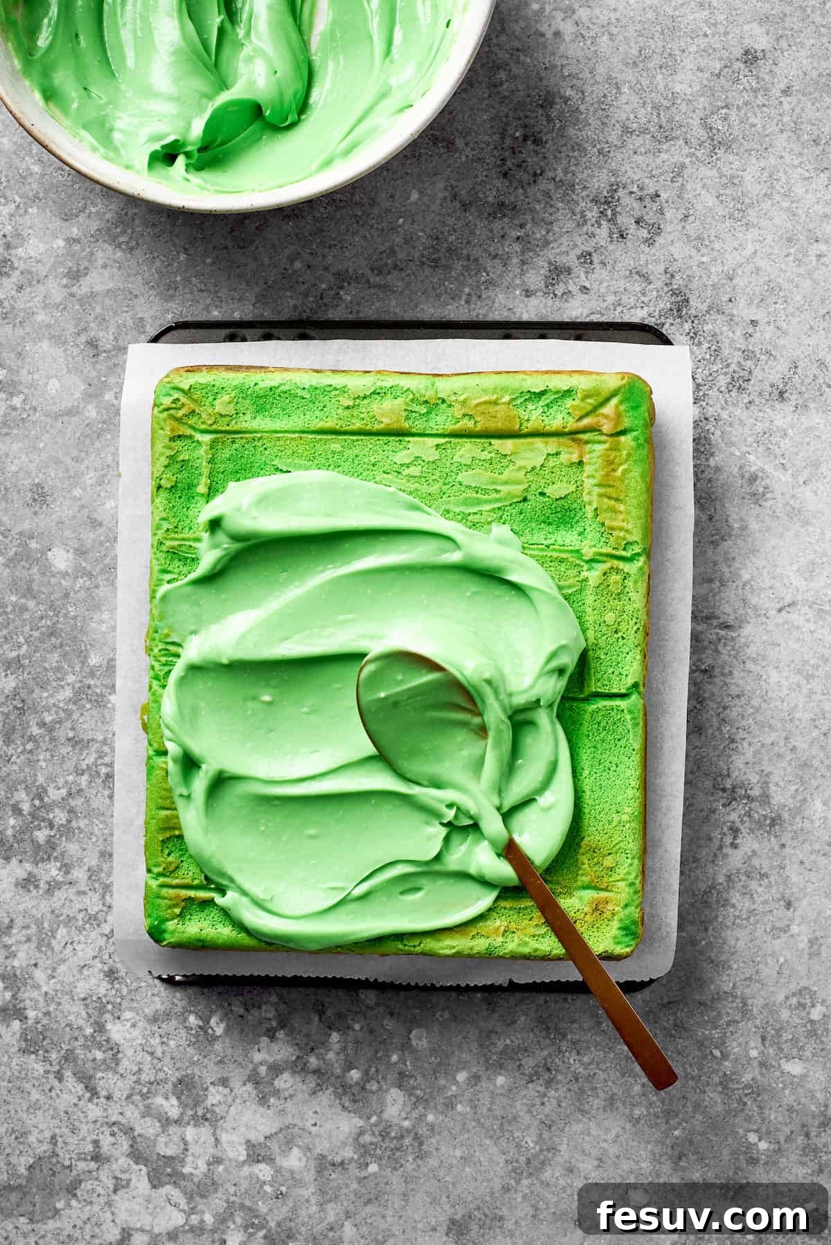 Green Grinch Cake features a tender, brightly-hued vanilla cake topped with tangy cream cheese frosting and studded with bits of candy. Green icing is added to the top of a baked cake.