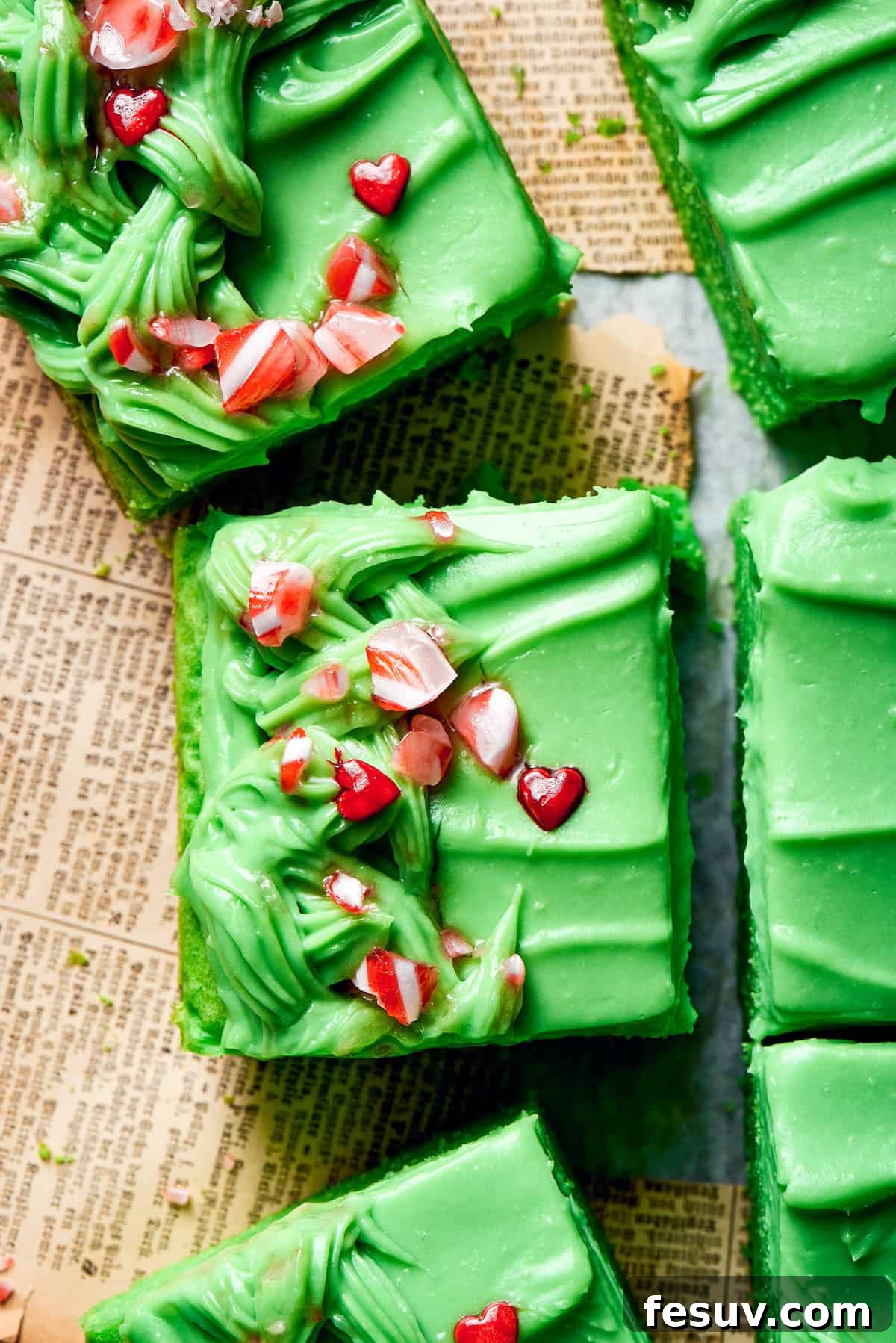 Green Grinch Cake features a tender, brightly-hued vanilla cake topped with tangy cream cheese frosting and studded with bits of candy. Crushed candy tops slices of grinch cake.