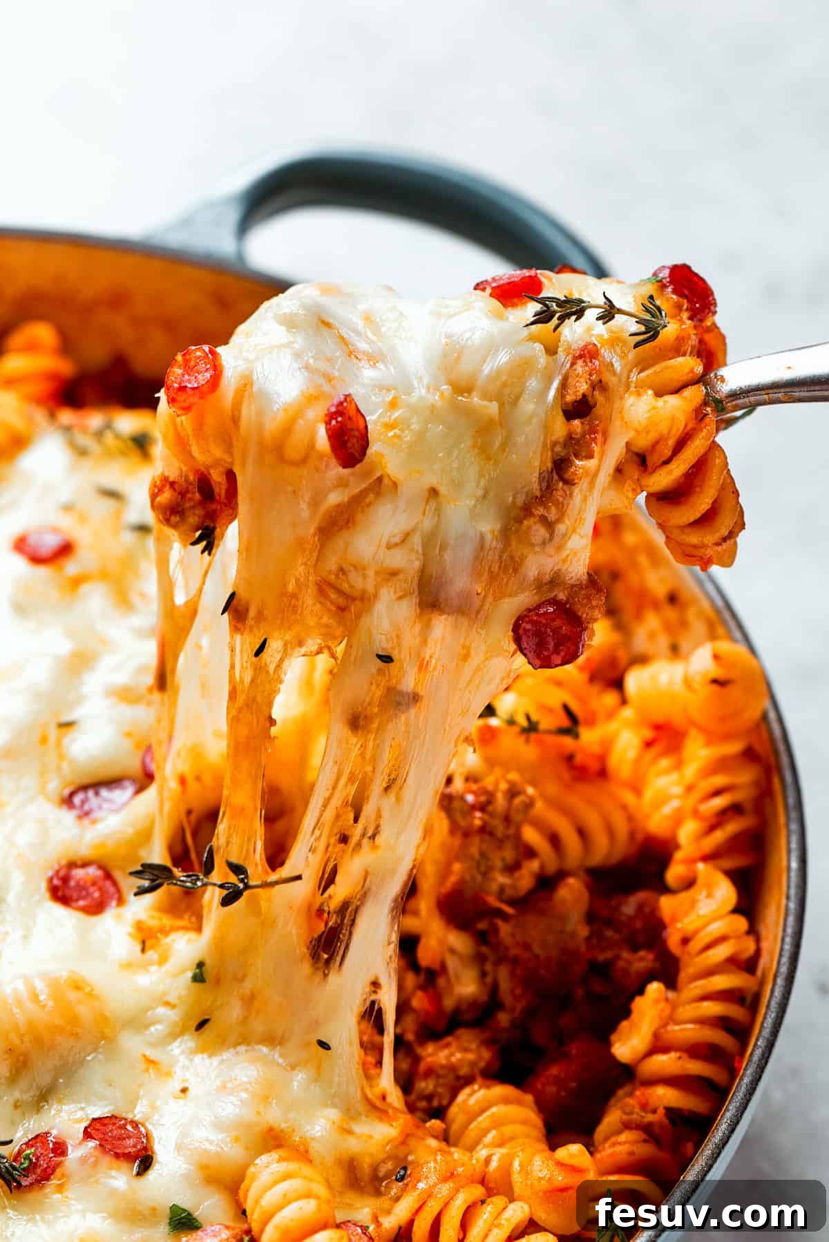 A generous serving of cheesy pizza pasta being pulled from a skillet, showcasing the stretchy mozzarella and chunky ingredients.