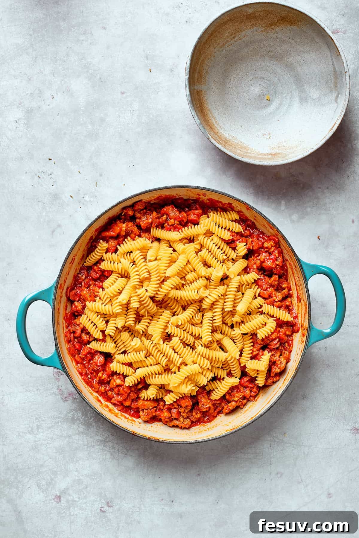 Rotini pasta is added to the skillet filled with the savory sausage and tomato sauce mixture.