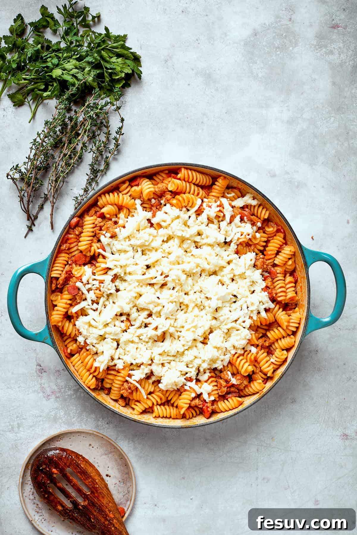 Shredded mozzarella cheese is generously sprinkled over the cooked pizza pasta in the skillet.