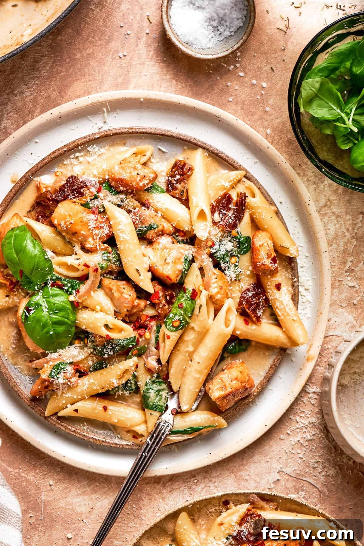 A large plate of Marry Me Chicken Pasta, garnished with fresh basil leaves, ready to be served. The creamy sauce, tender chicken, and vibrant sun-dried tomatoes are clearly visible.