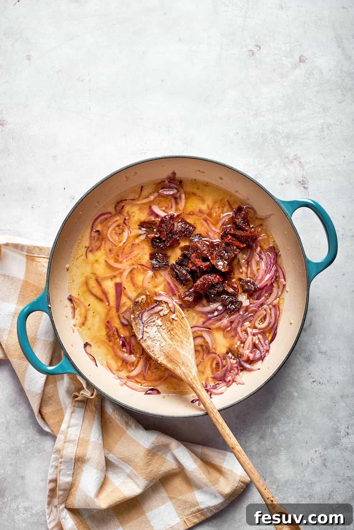 Chopped sun-dried tomatoes being stirred into a simmering liquid of chicken broth and white wine in a skillet.