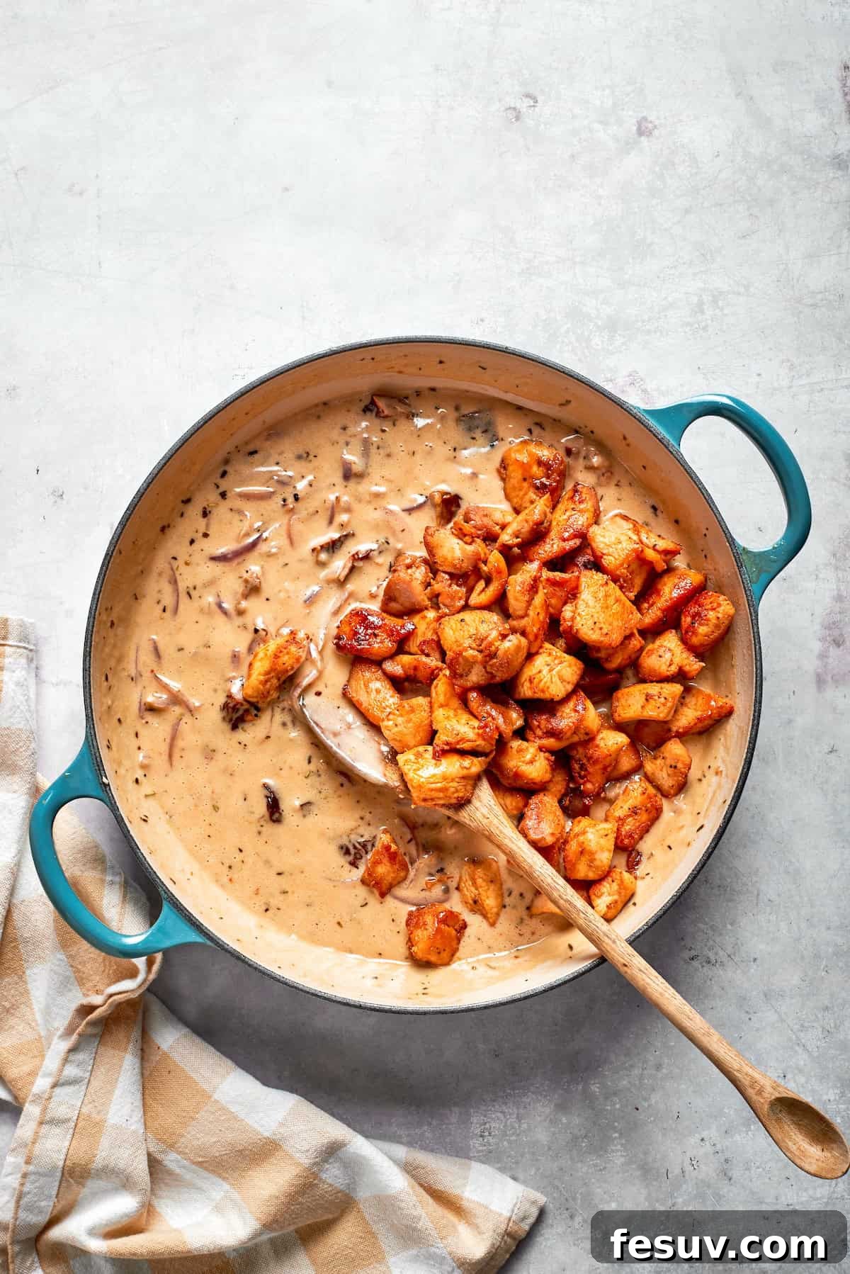Cooked chicken pieces being stirred back into the creamy sauce in the skillet.