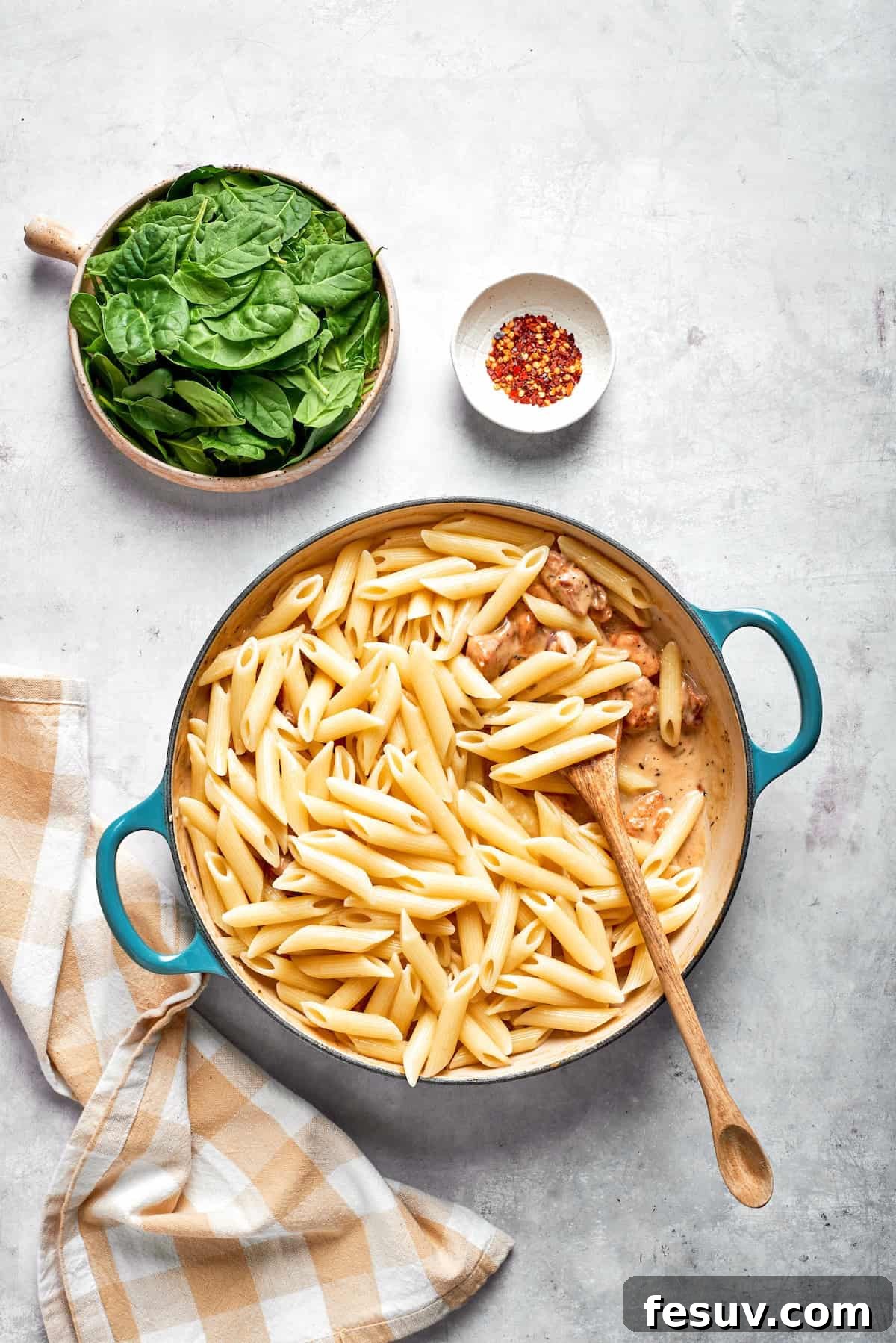 Al dente penne pasta being tossed with the creamy chicken and sun-dried tomato sauce in a large skillet, ensuring even coating.
