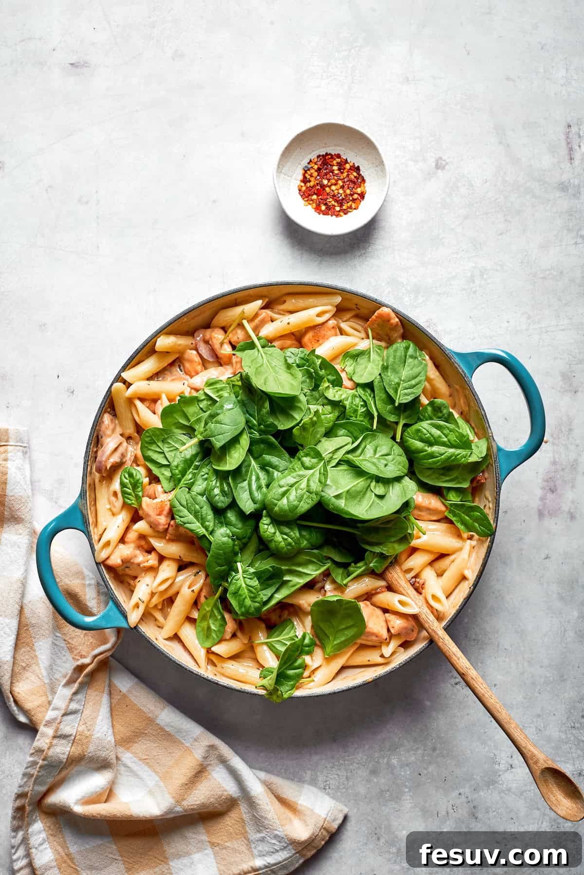 Fresh spinach leaves wilting into the hot Marry Me Chicken Pasta in the skillet, adding a vibrant green color.