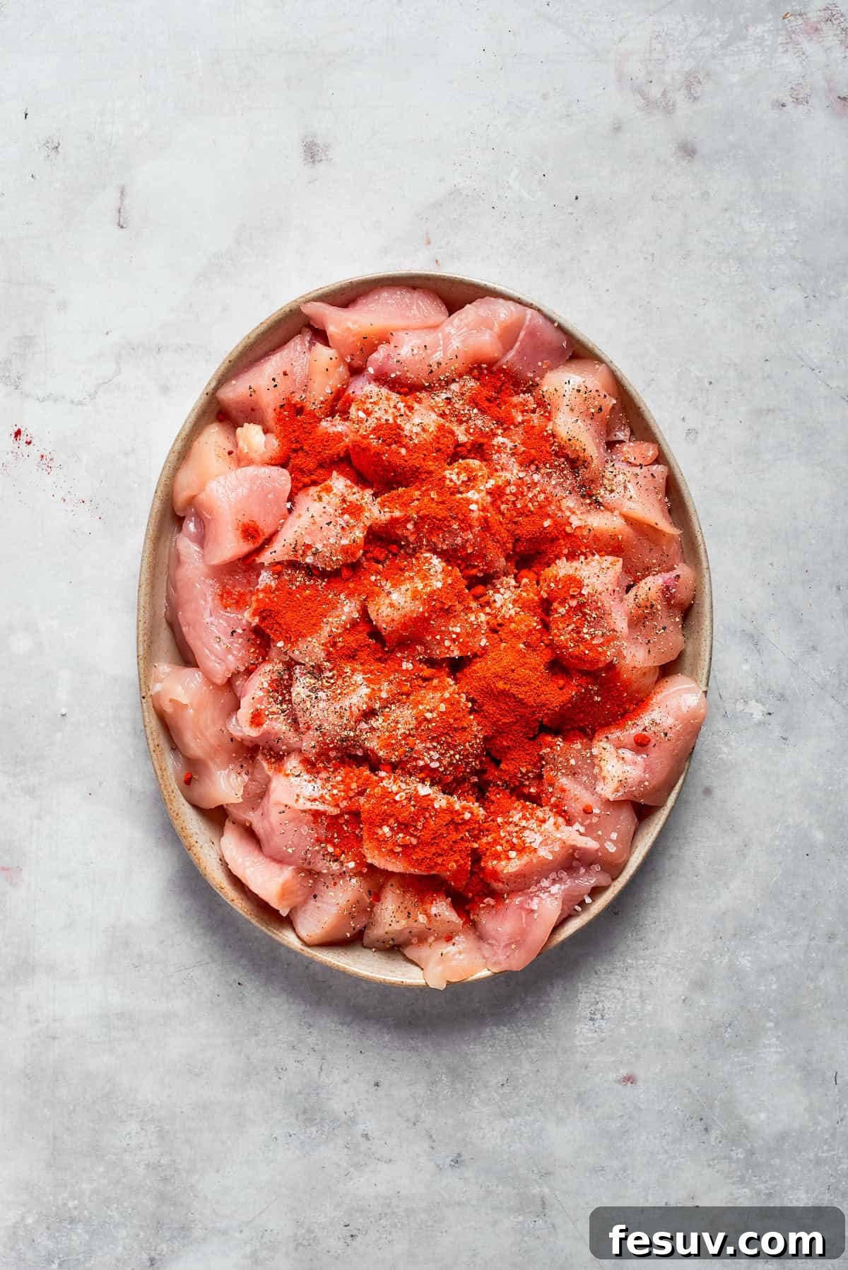 Diced chicken pieces seasoned generously with salt, pepper, and paprika on a white plate, ready for searing.