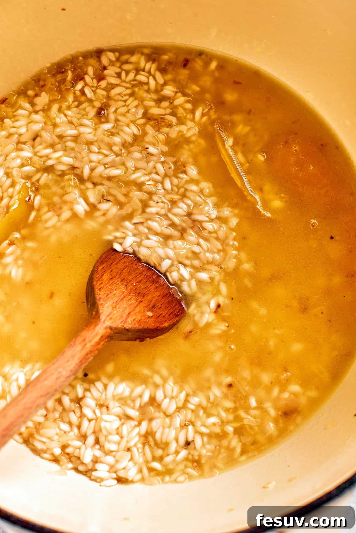 Ladle by ladle, adding warm broth to the rice and stirring constantly.