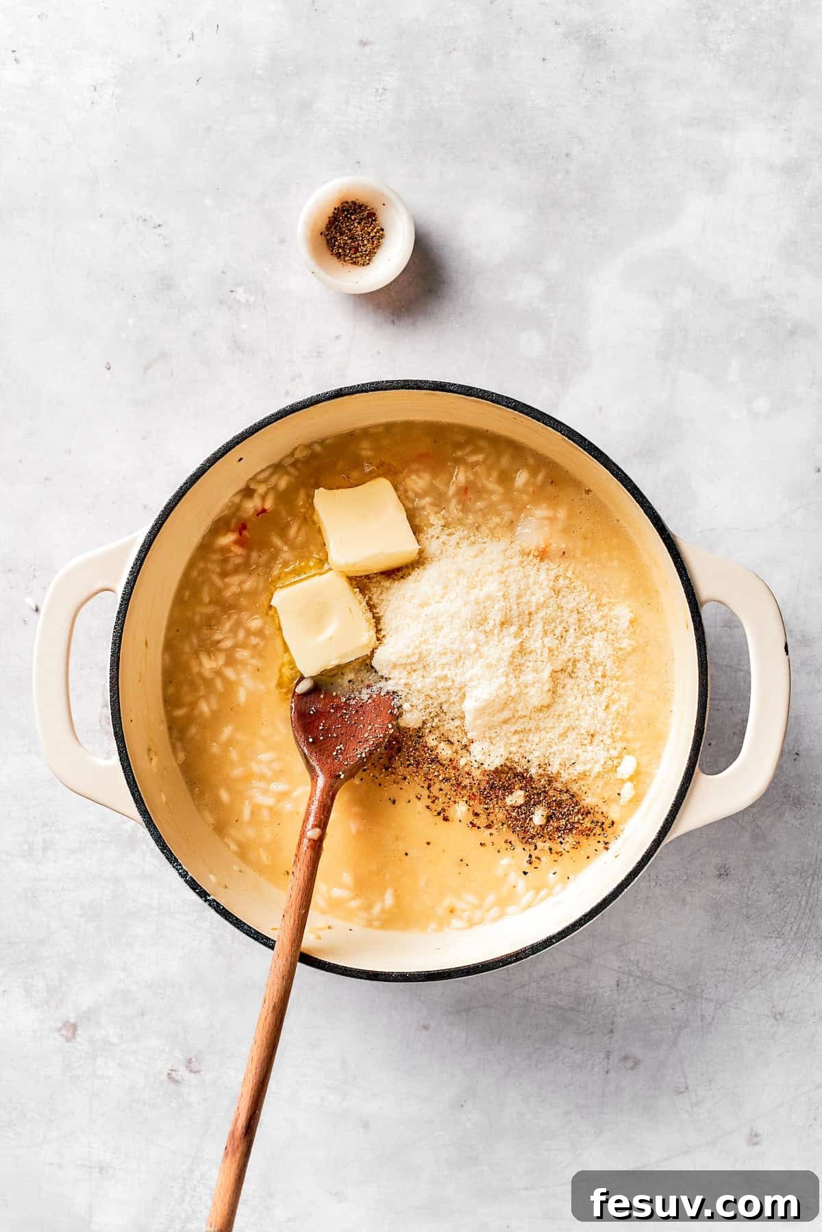 Finishing the risotto by stirring in butter and grated Parmesan cheese.
