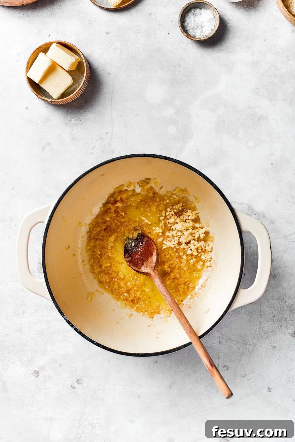 Stirring aromatics like shallots and garlic in a pot with olive oil and butter.