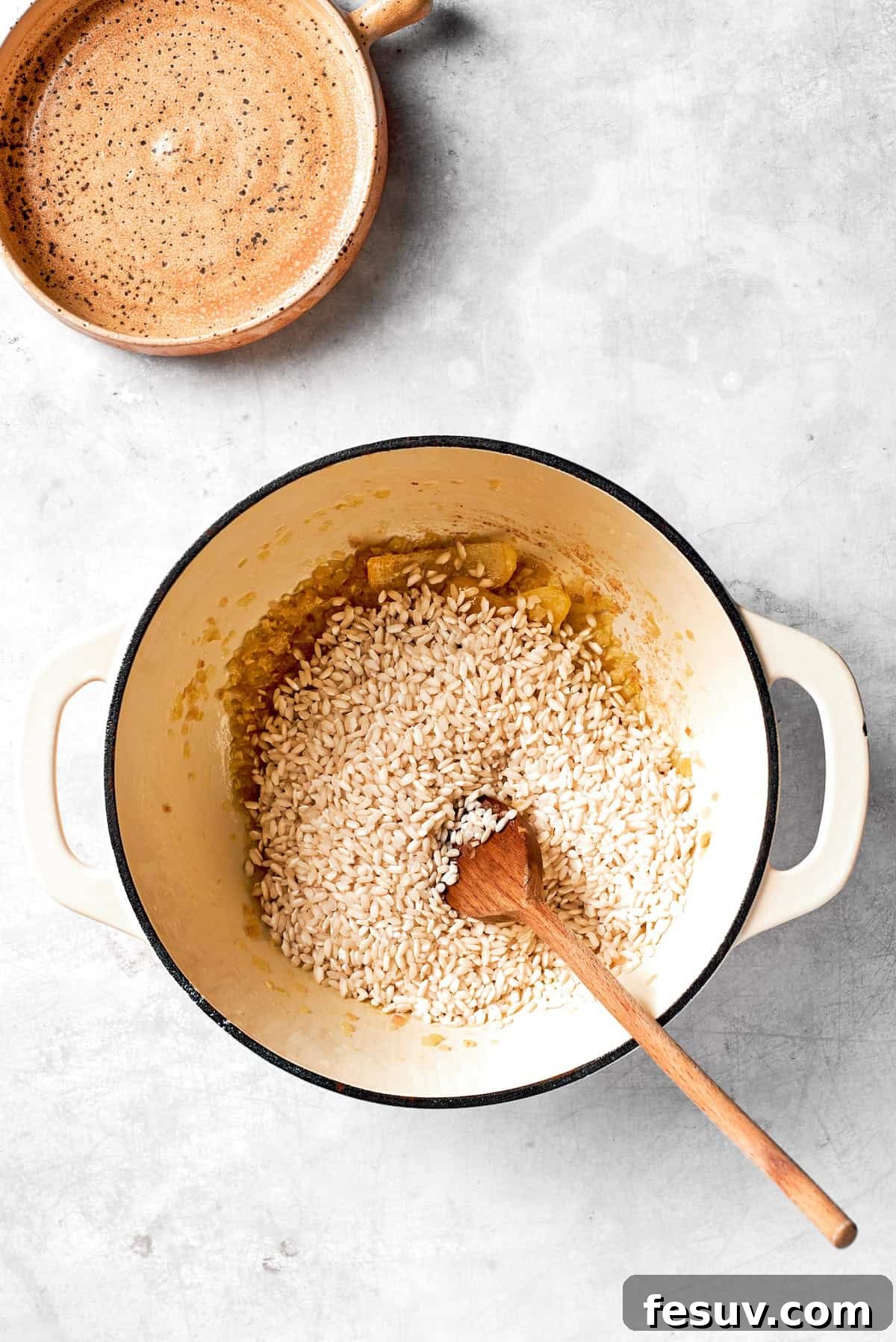 Adding risotto rice to the pot with sautéed aromatics and stirring to toast the grains.