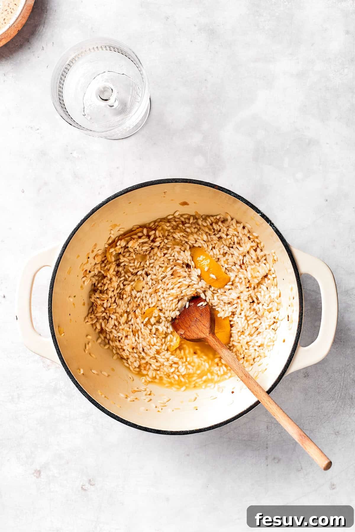 Pouring dry white wine into the pot with the toasted rice to deglaze.