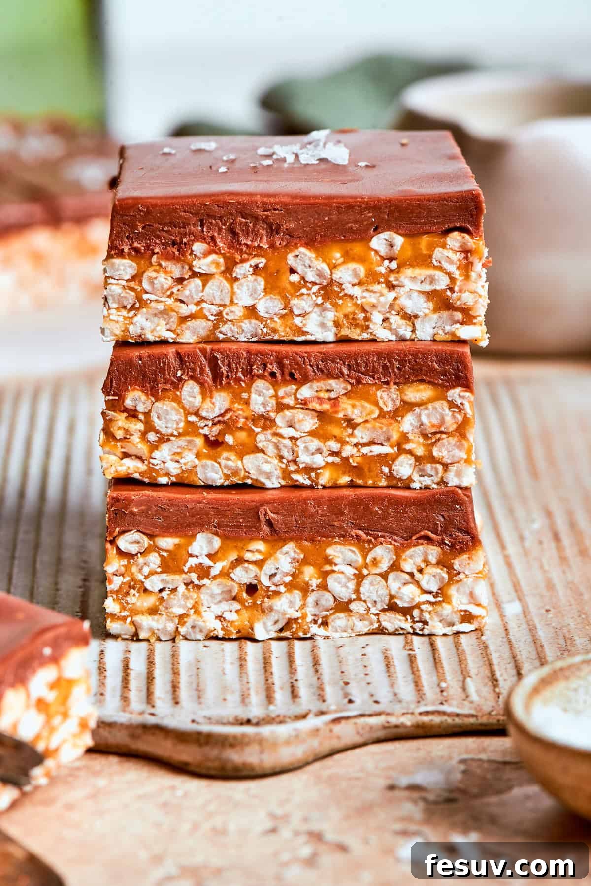 No-bake scotcharoos feature creamy peanut butter, crispy rice cereal, and a sweet layer of melted chocolate and butterscotch. Three scotcharoos stacked on top of each other, showcasing their layers.