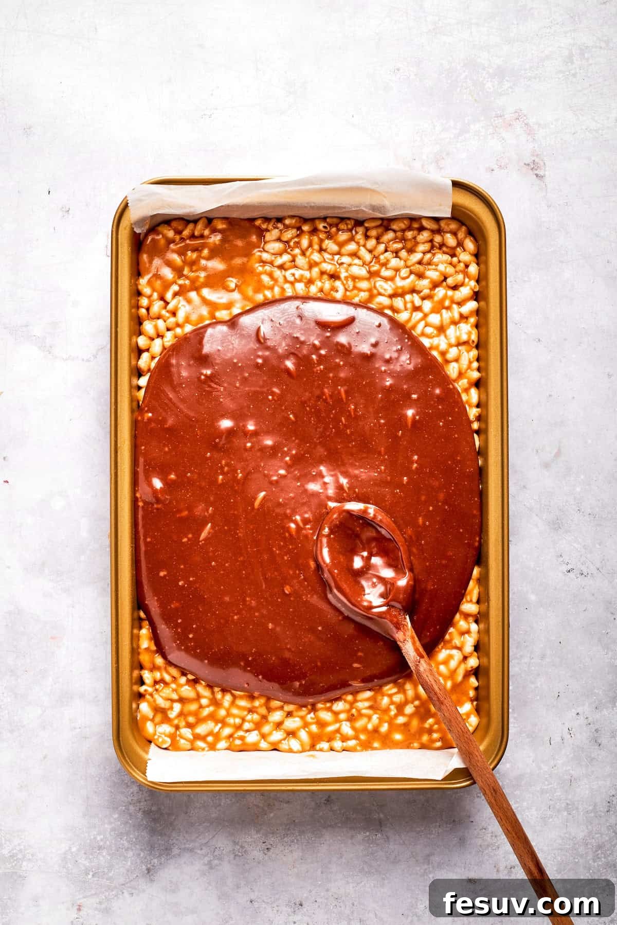Golden Peanut Butter Crunch Bars 8 Melted chocolate and butterscotch mixture being spread smoothly over the cereal base in a baking pan.
