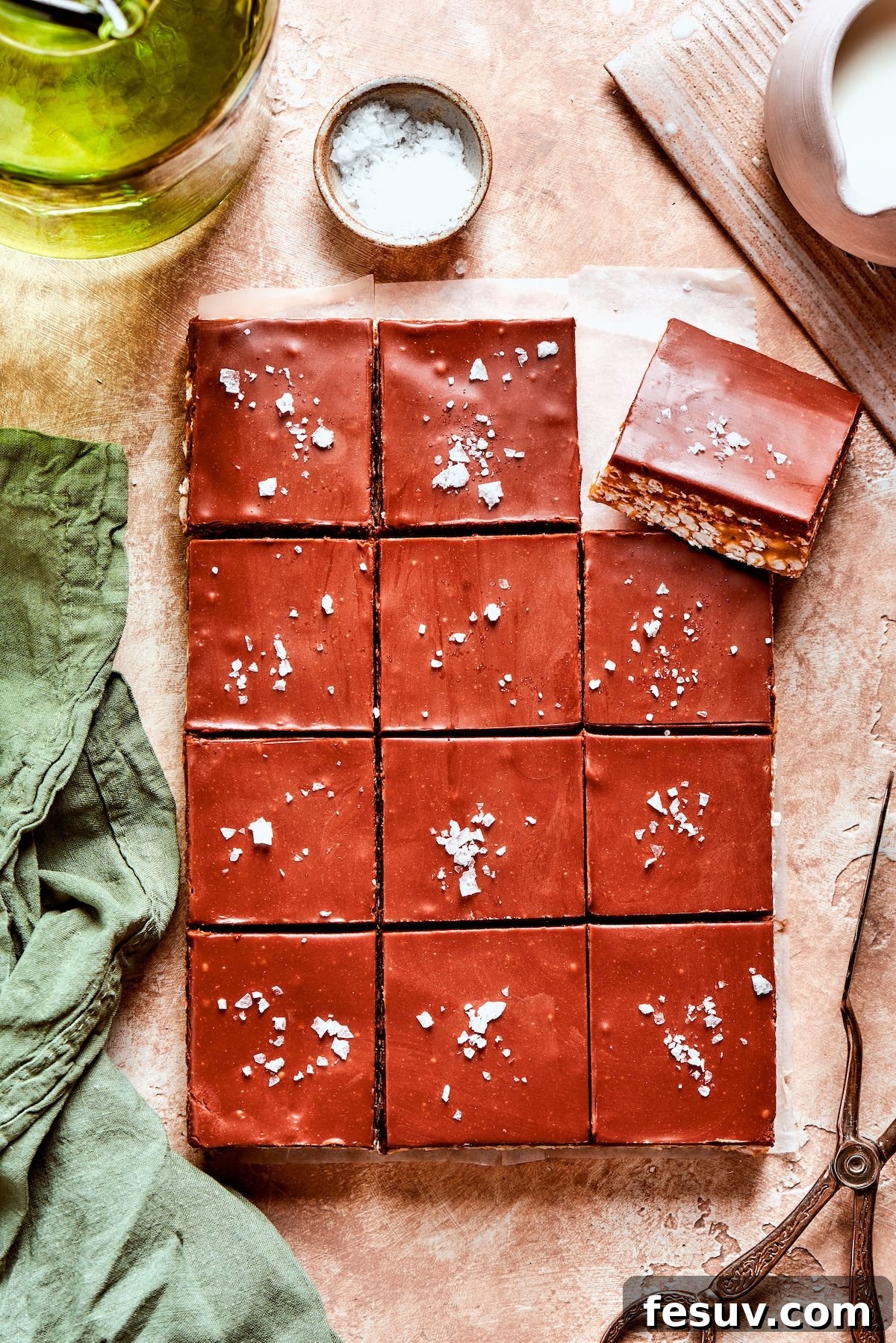 No-bake scotcharoos feature creamy peanut butter, crispy rice cereal, and a sweet layer of melted chocolate and butterscotch. Flaky salt is meticulously added to a dozen freshly made scotcharoos.