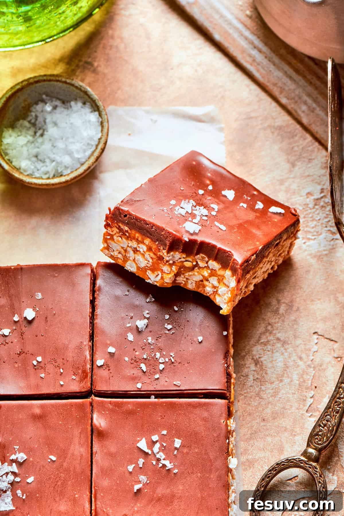 No-bake scotcharoos feature creamy peanut butter, crispy rice cereal, and a sweet layer of melted chocolate and butterscotch. A Scotcharoo with a delicious bite taken out, showing the layers.