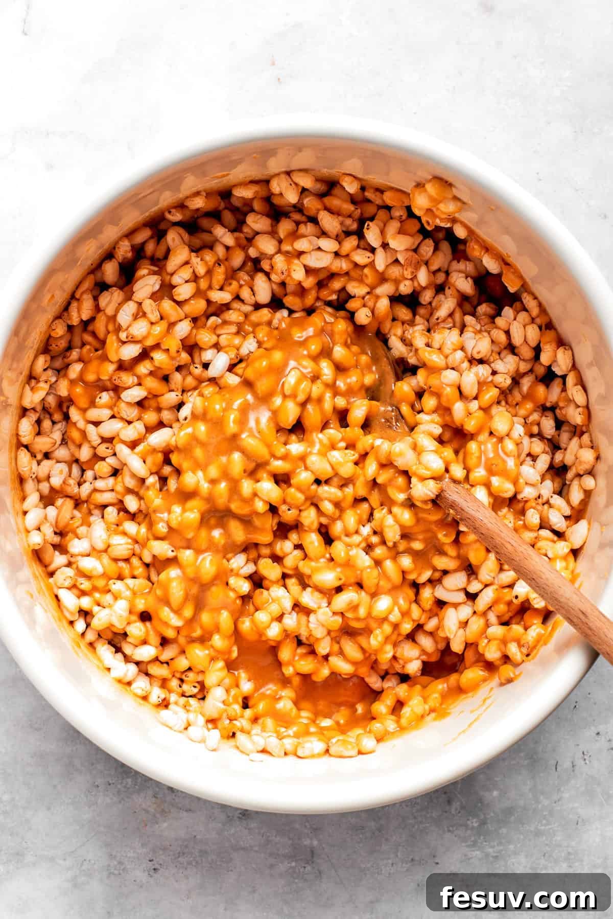 Golden Peanut Butter Crunch Bars 5 The peanut butter mixture being poured over crispy rice cereal in a large mixing bowl.