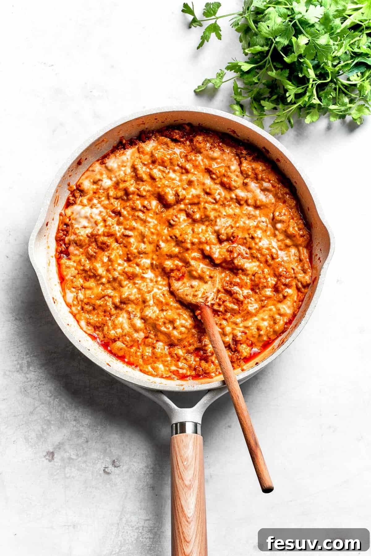 The creamy, seasoned ground beef mixture for Dorito casserole, ready to be layered, in a skillet with a serving spoon.