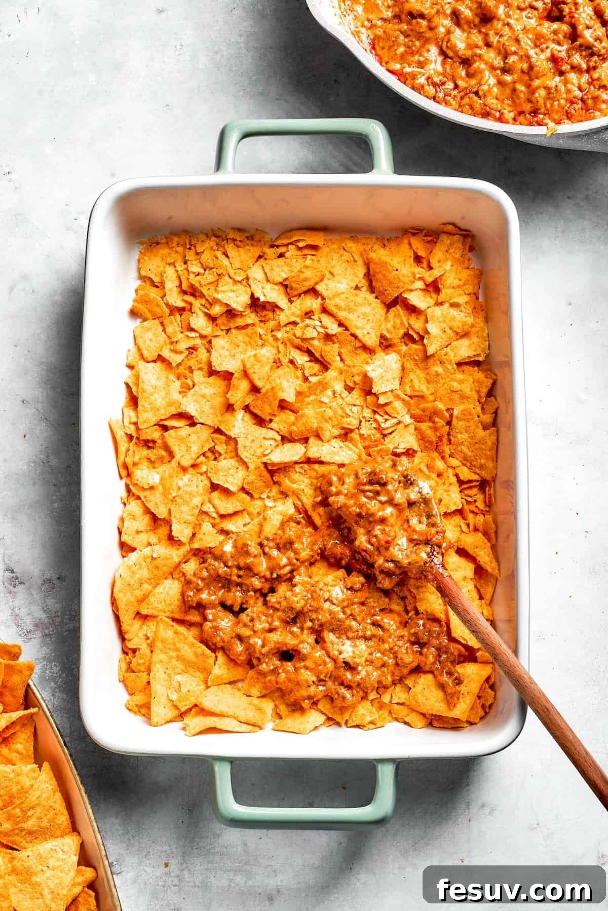 A casserole dish with a base layer of crushed Doritos, being topped with a generous portion of the creamy ground beef filling.
