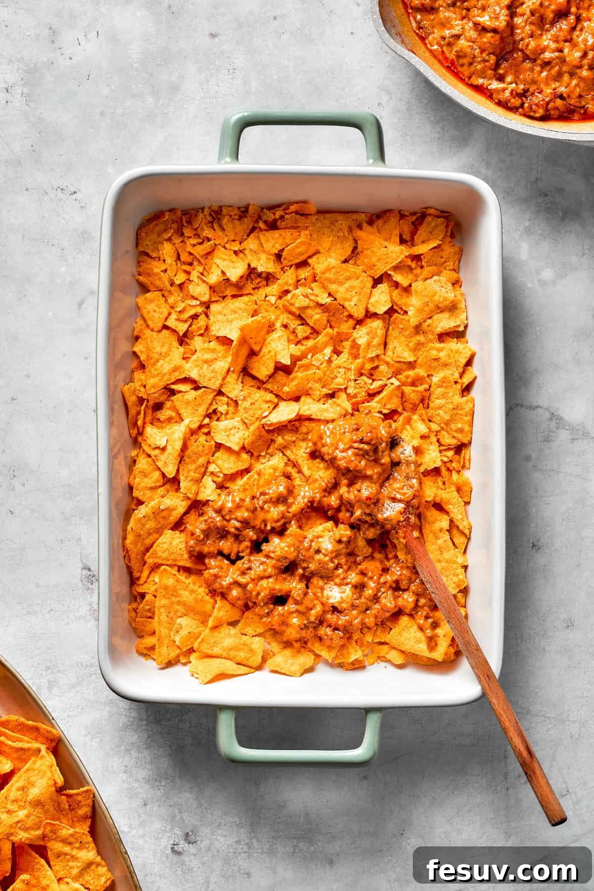The first layer of creamy ground beef filling spread over crushed Doritos in a casserole dish, ready for cheese.