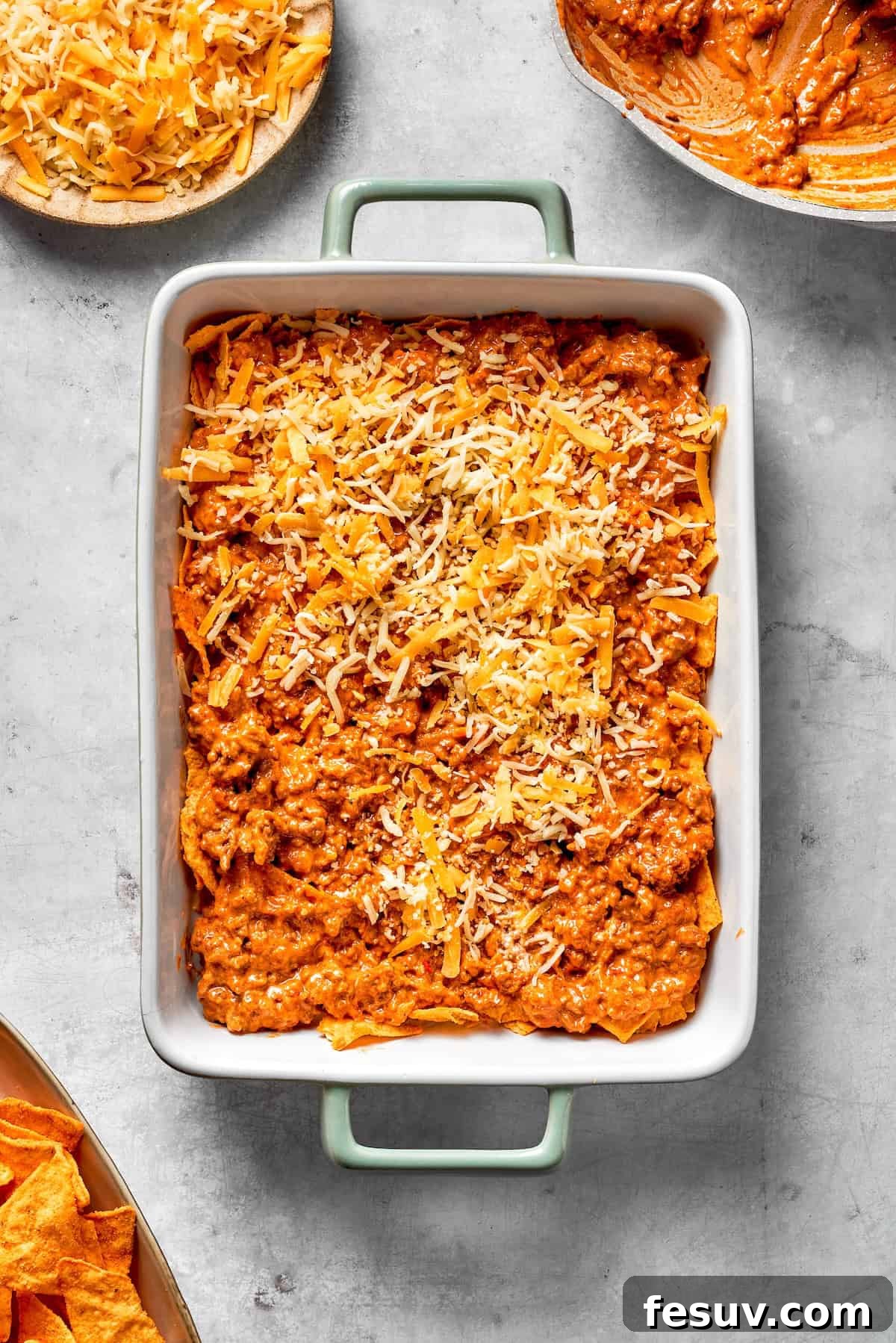 Generous shredded cheese being sprinkled over the top layer of a Dorito casserole, ready for baking.