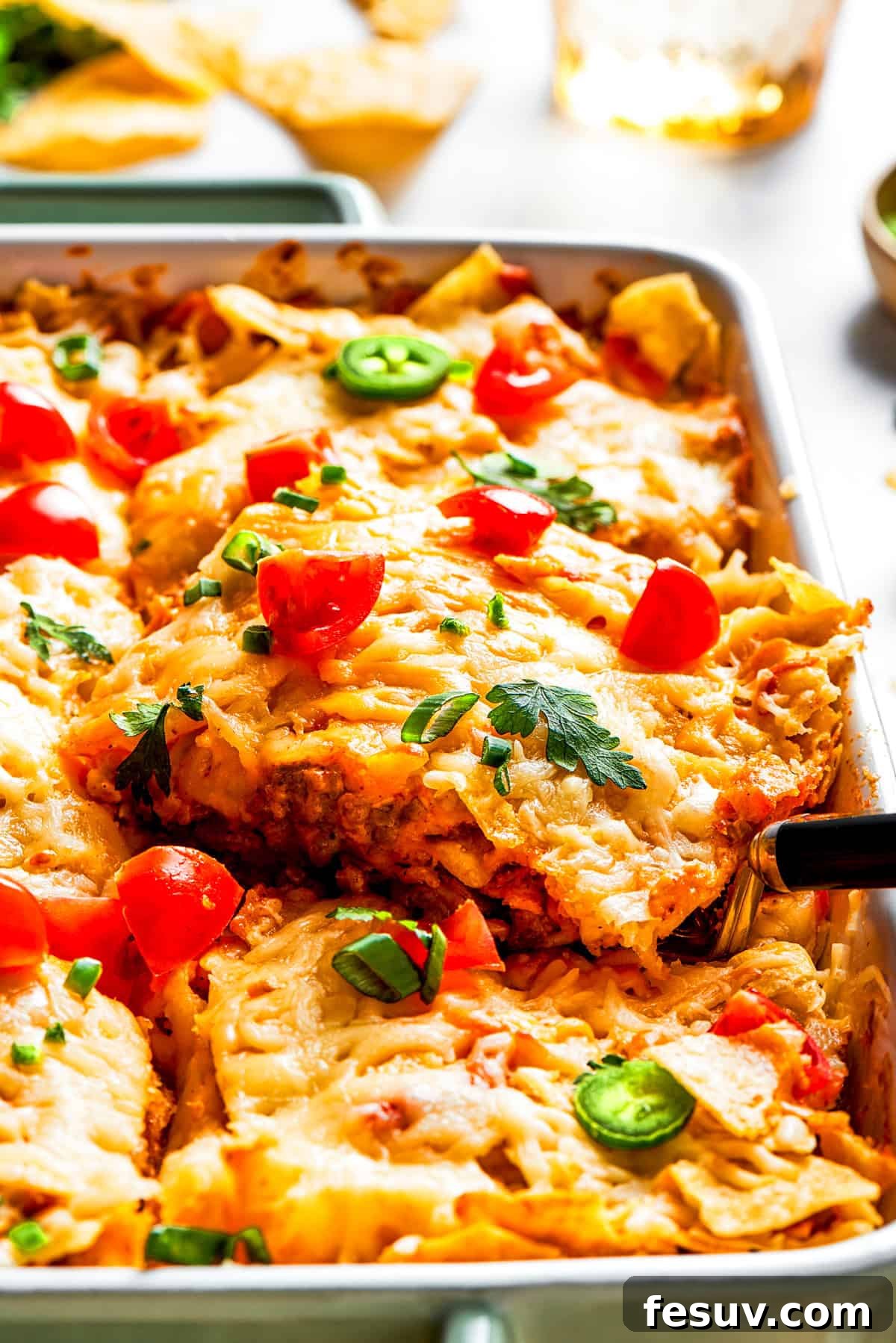 A vibrant side shot of a Dorito casserole topped with bubbling melted cheese, bright halved cherry tomatoes, and fresh green herbs like cilantro and green onions.