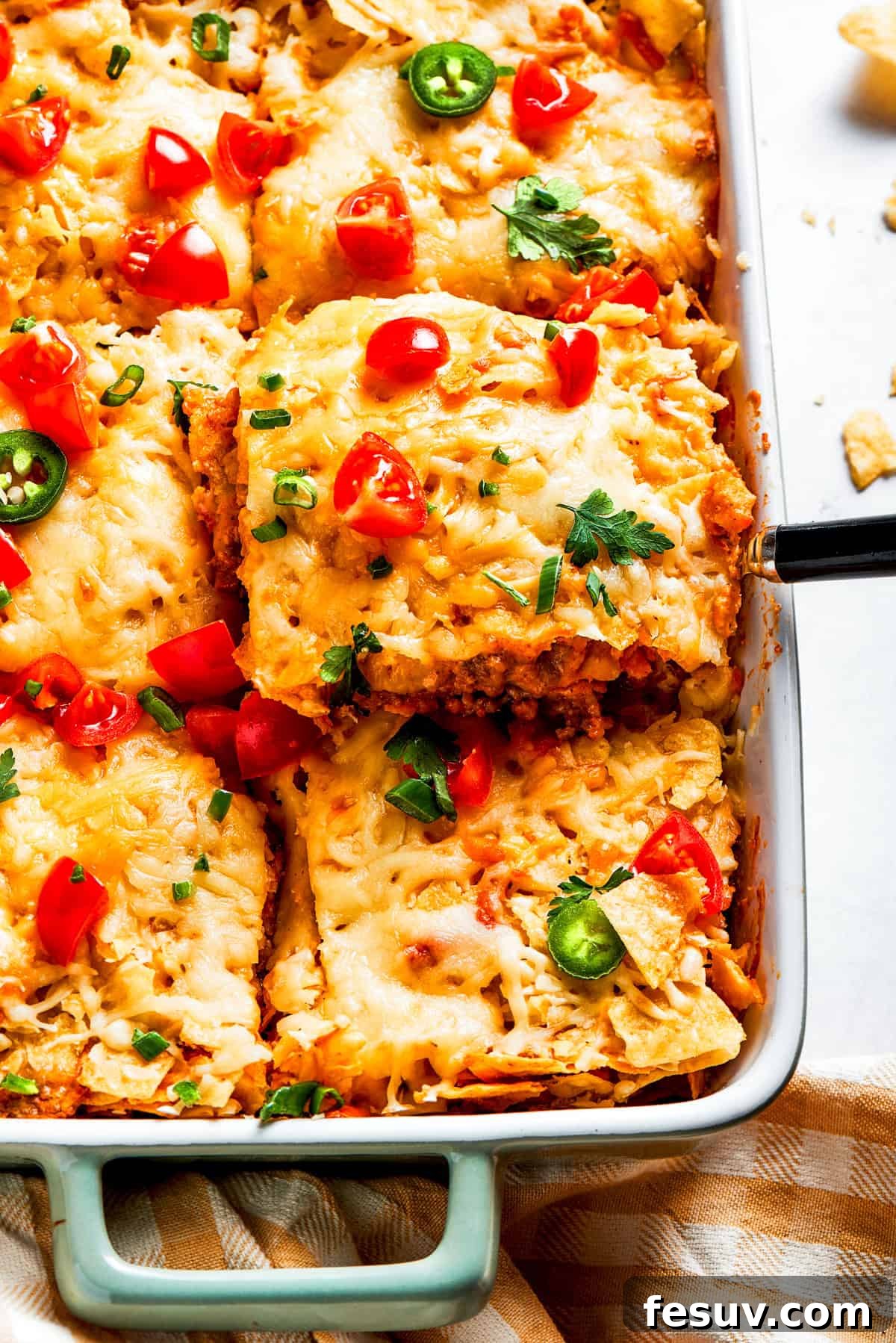 A serving utensil lifts a generous scoop of Dorito casserole, showcasing its delightful layers of crunchy chips, savory beef, and melted cheese, ready to be enjoyed.