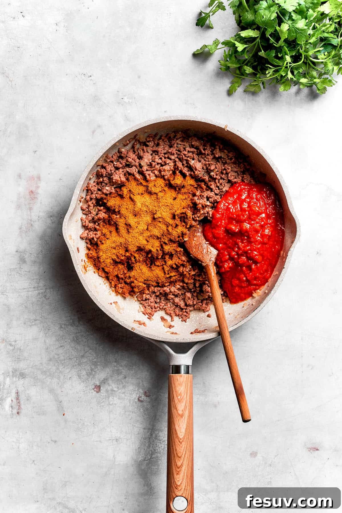 Diced onions and ground beef browning in a skillet on the stovetop, with taco seasoning ready to be added for flavor.