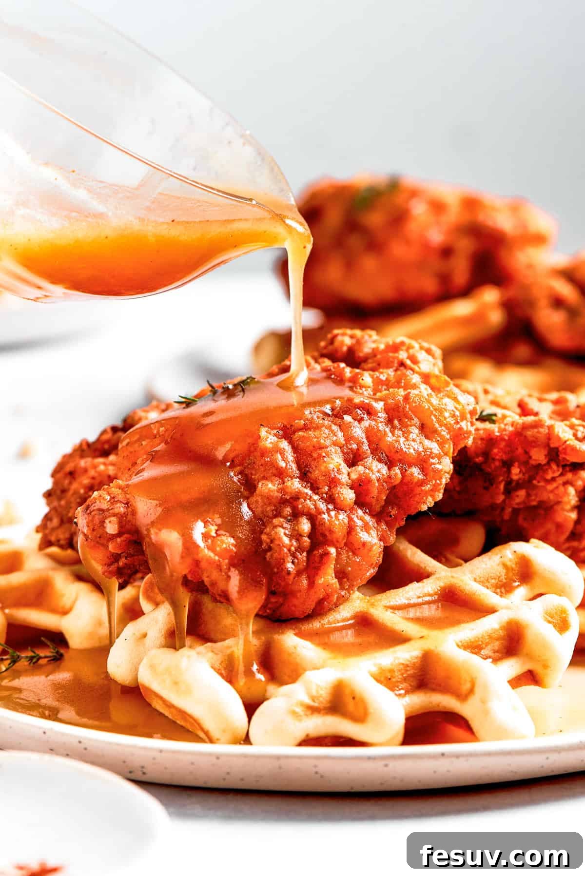 Drizzling Hot Honey Butter Sauce on Chicken and Waffles Pouring homemade hot honey butter sauce generously over crispy fried chicken and fluffy waffles.