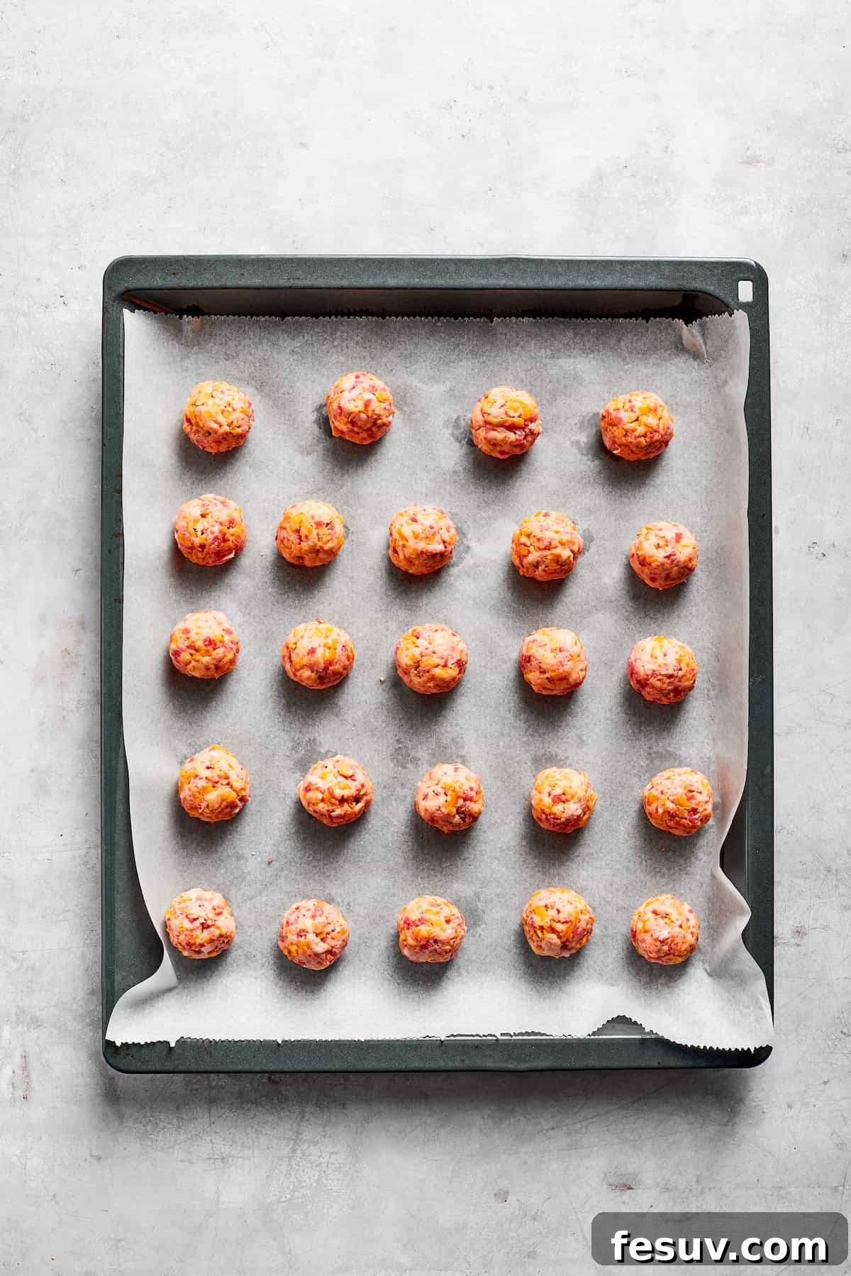 This sausage balls recipe relies on Bisquick, pork sausage, and Italian seasoning for an easy appetizer. Don't forget the dipping sauce! A lined baking tray with sausage balls.