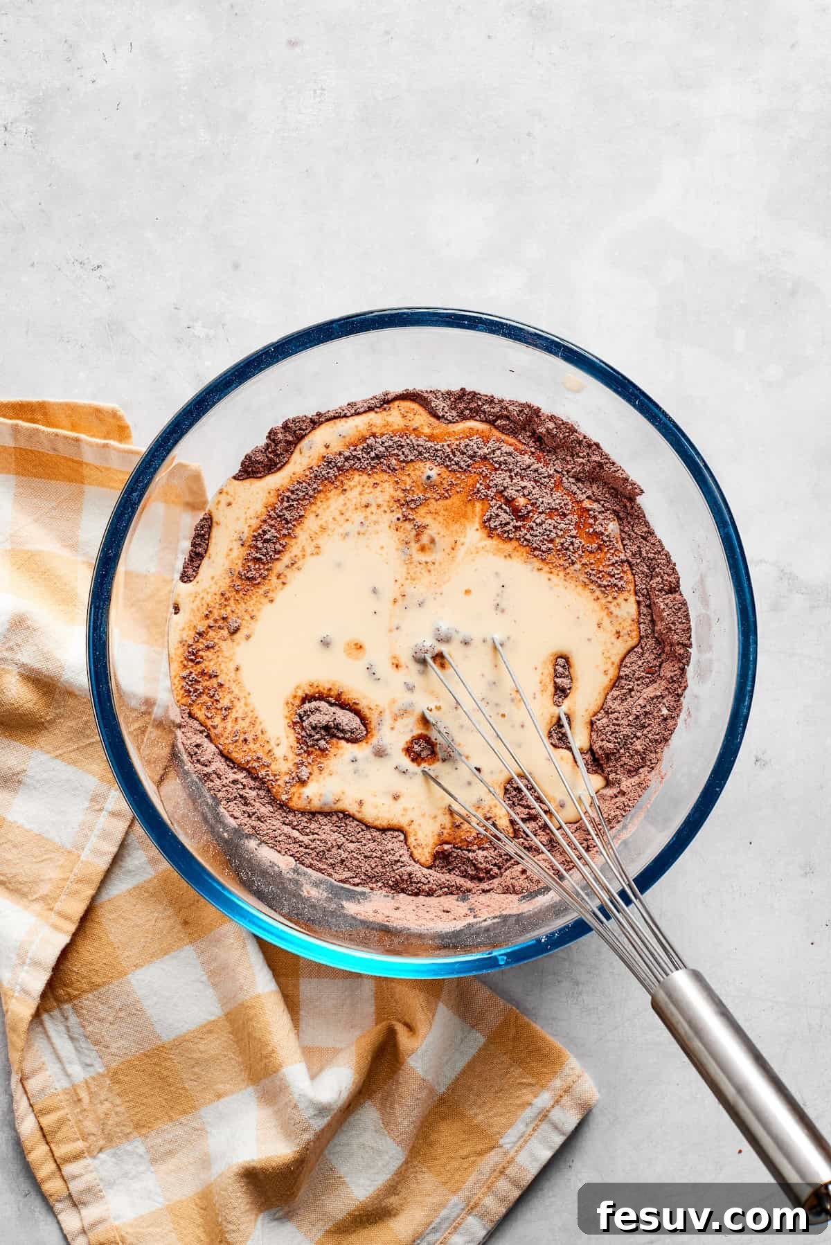 Dry and wet ingredients for chocolate muffins are being gently whisked together in a bowl, creating the batter.