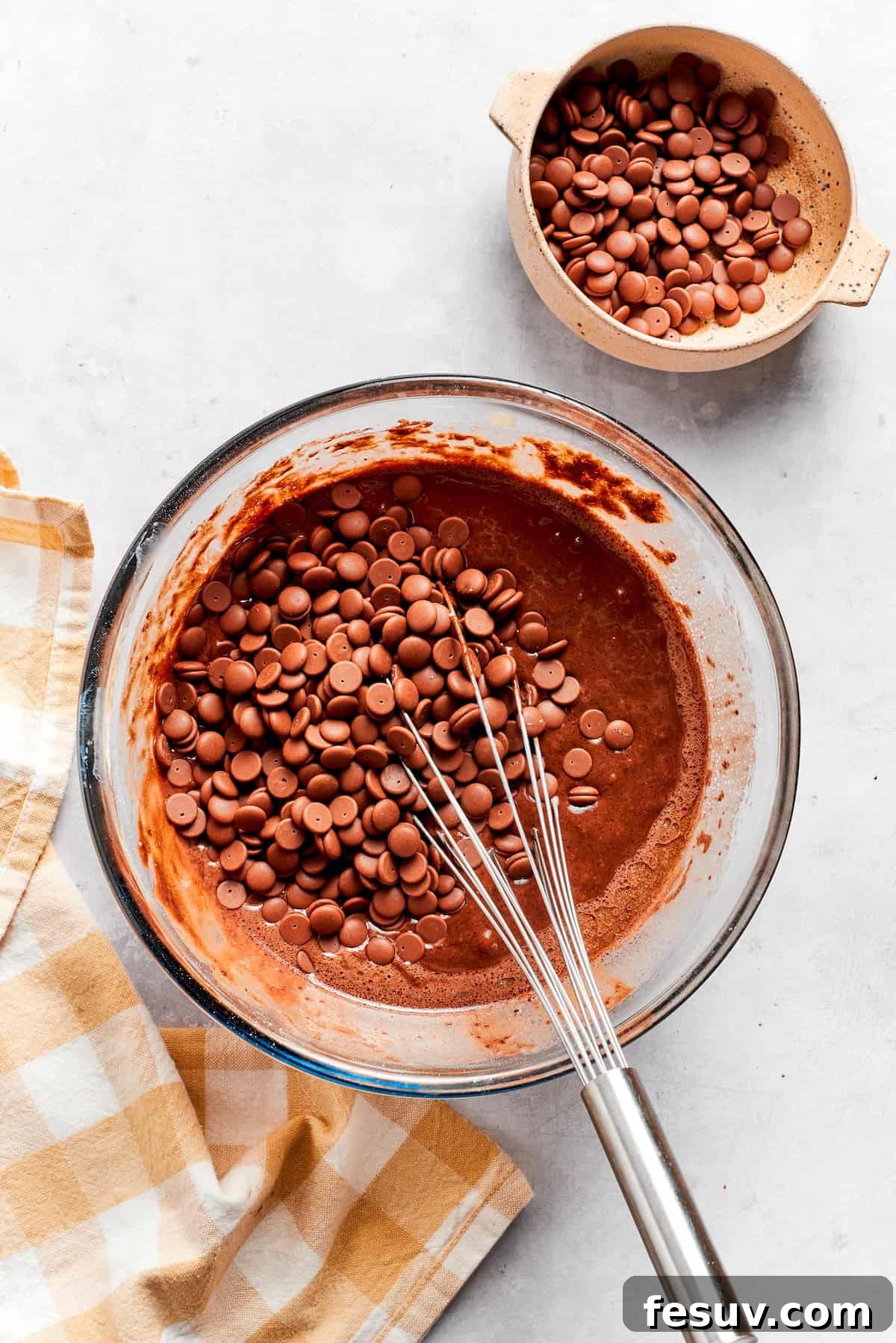 Abundant chocolate chips are being folded into the smooth chocolate muffin batter in a large bowl.